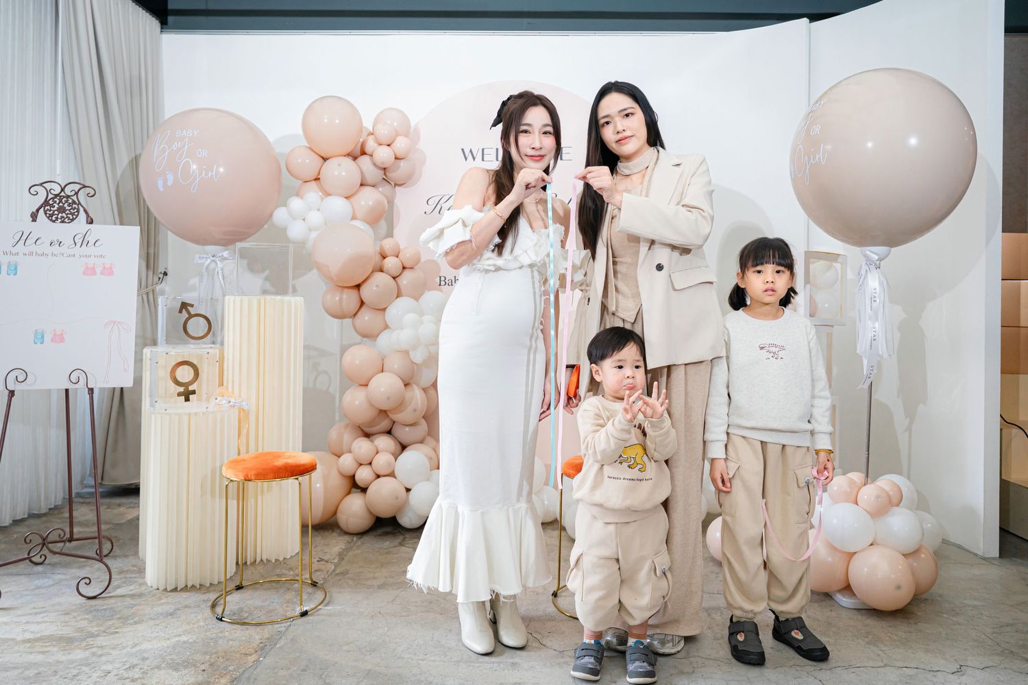Family in coordinated neutral outfits poses together against balloon arch backdrop during indoor photo session.