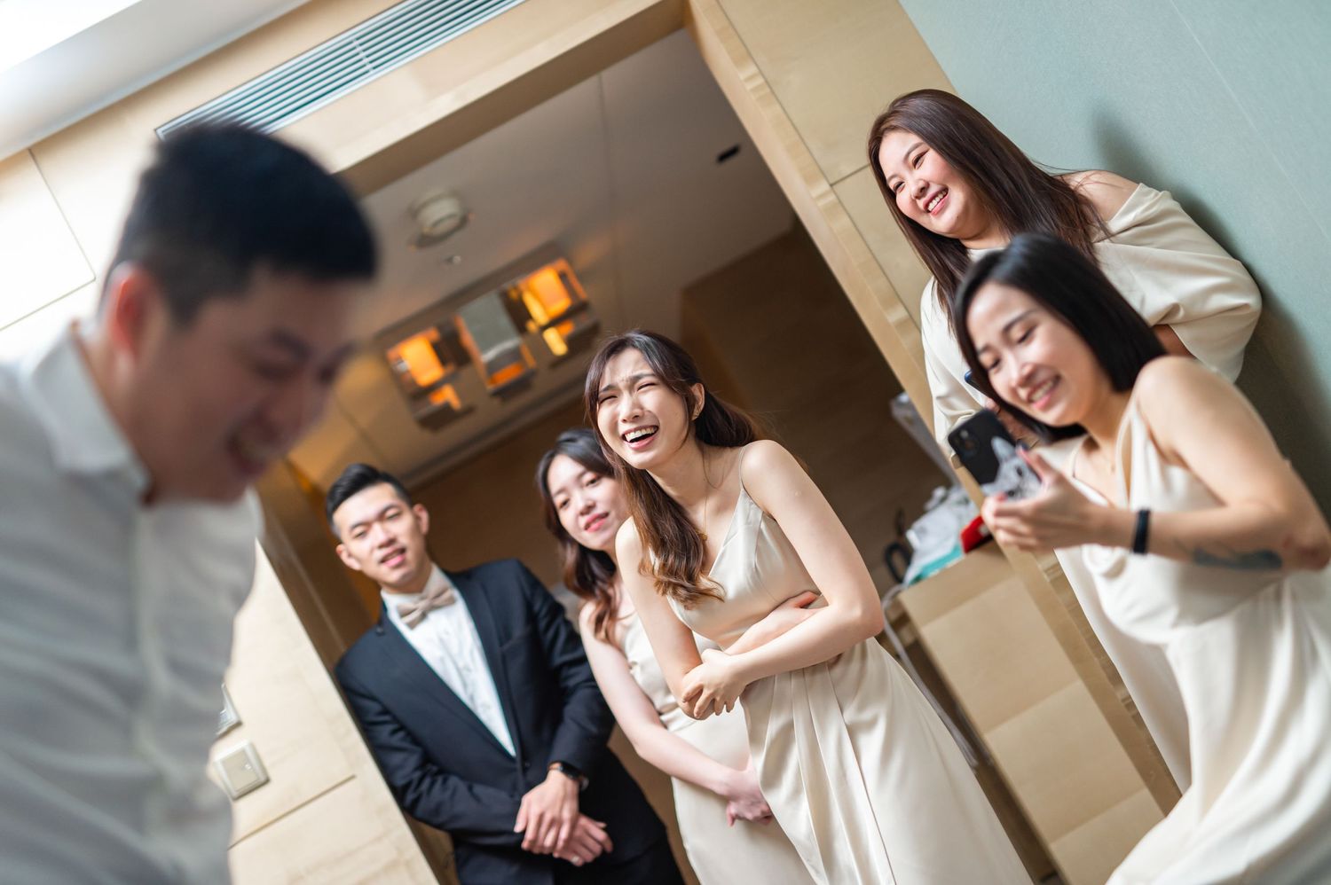 A group dressed in formal attire shares a candid laughing moment together in an indoor venue.