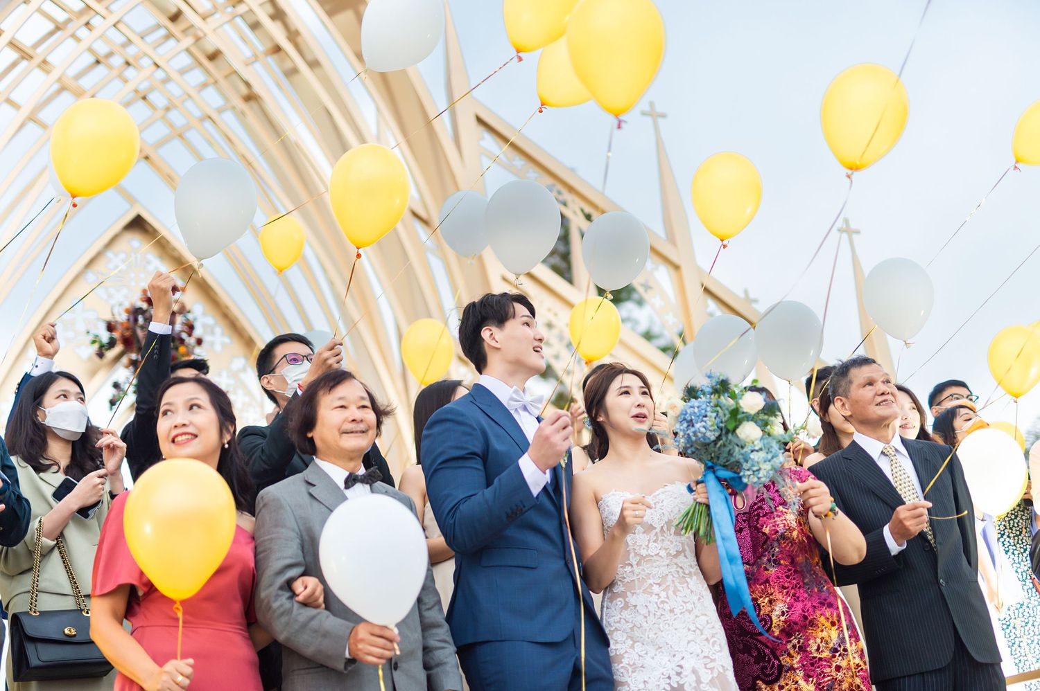 Wedding celebration with guests releasing bright yellow balloons into the air during a joyful outdoor ceremony.