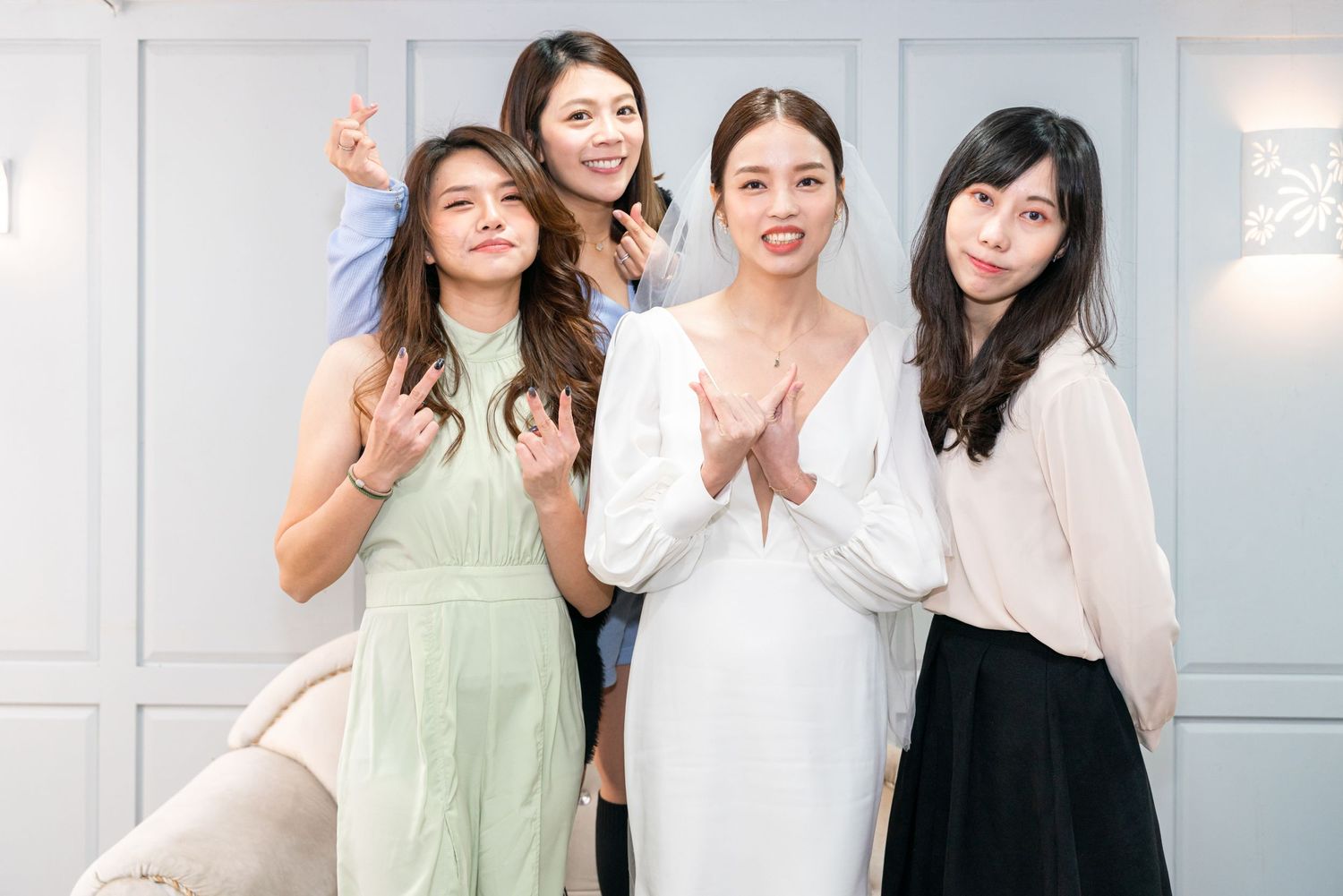 Four friends pose together at a celebration, wearing elegant dresses in pastel green, white and black colors.