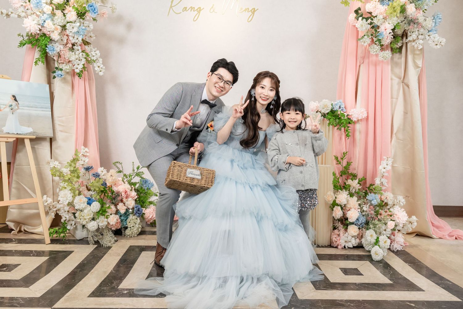 A family in matching blue formal attire poses together in an elegant studio setting with floral decorations.