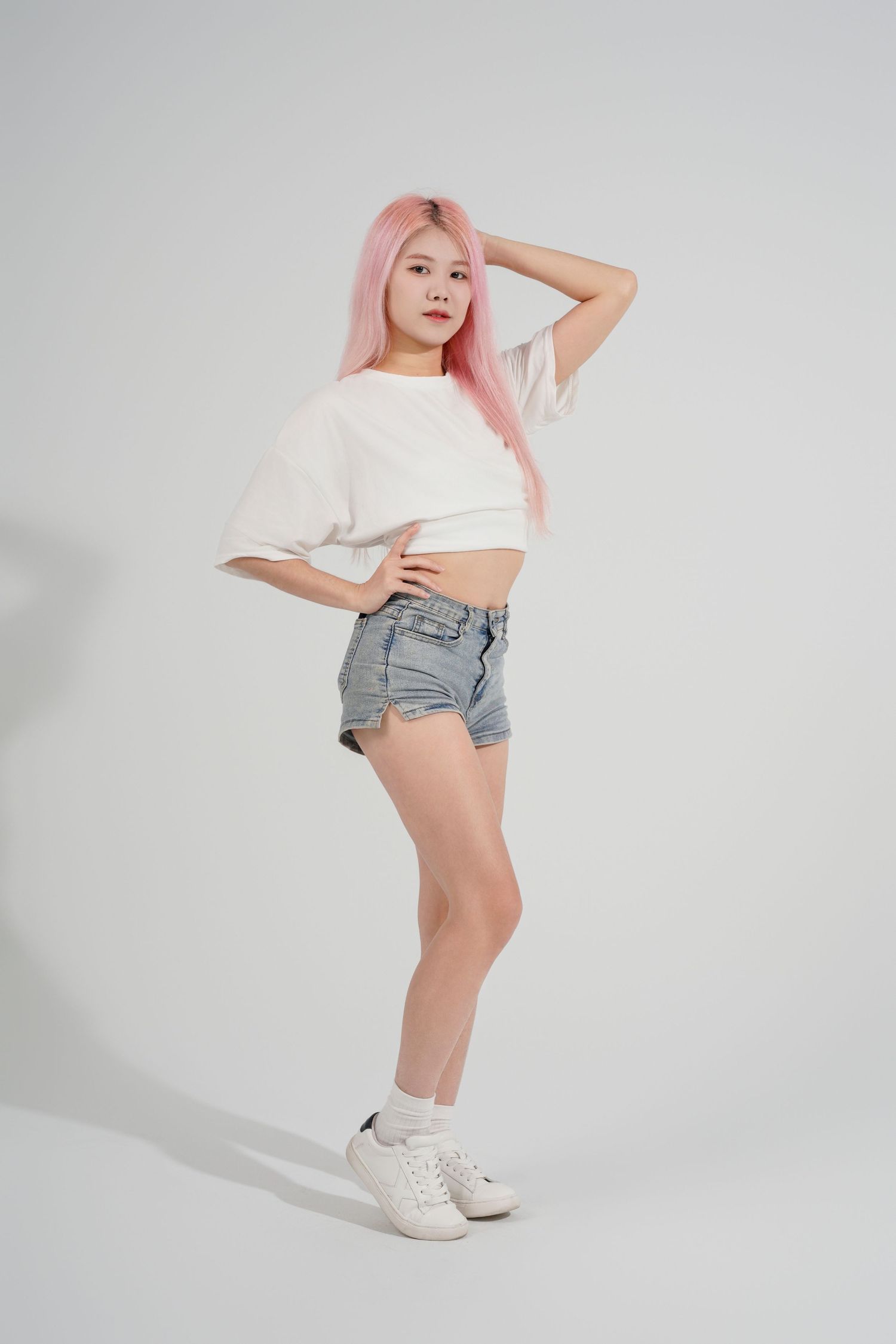 Fashion model in white crop top and denim shorts poses against light gray background in multiple dynamic poses.