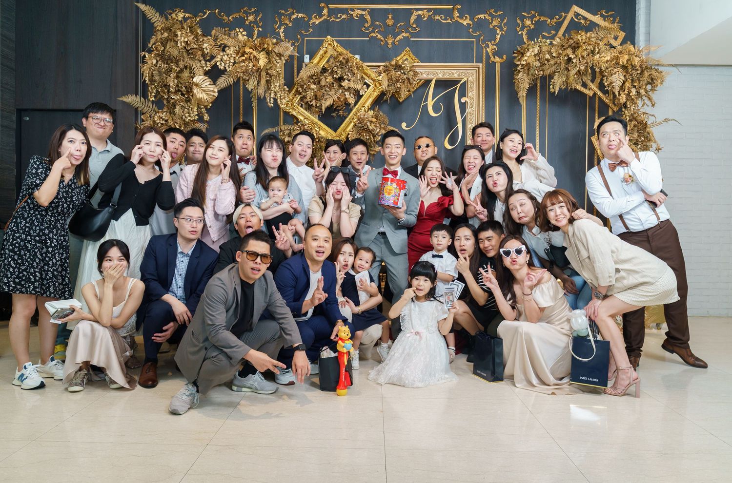 A large group poses together for a celebratory photo in front of an ornate gold backdrop at an event venue.