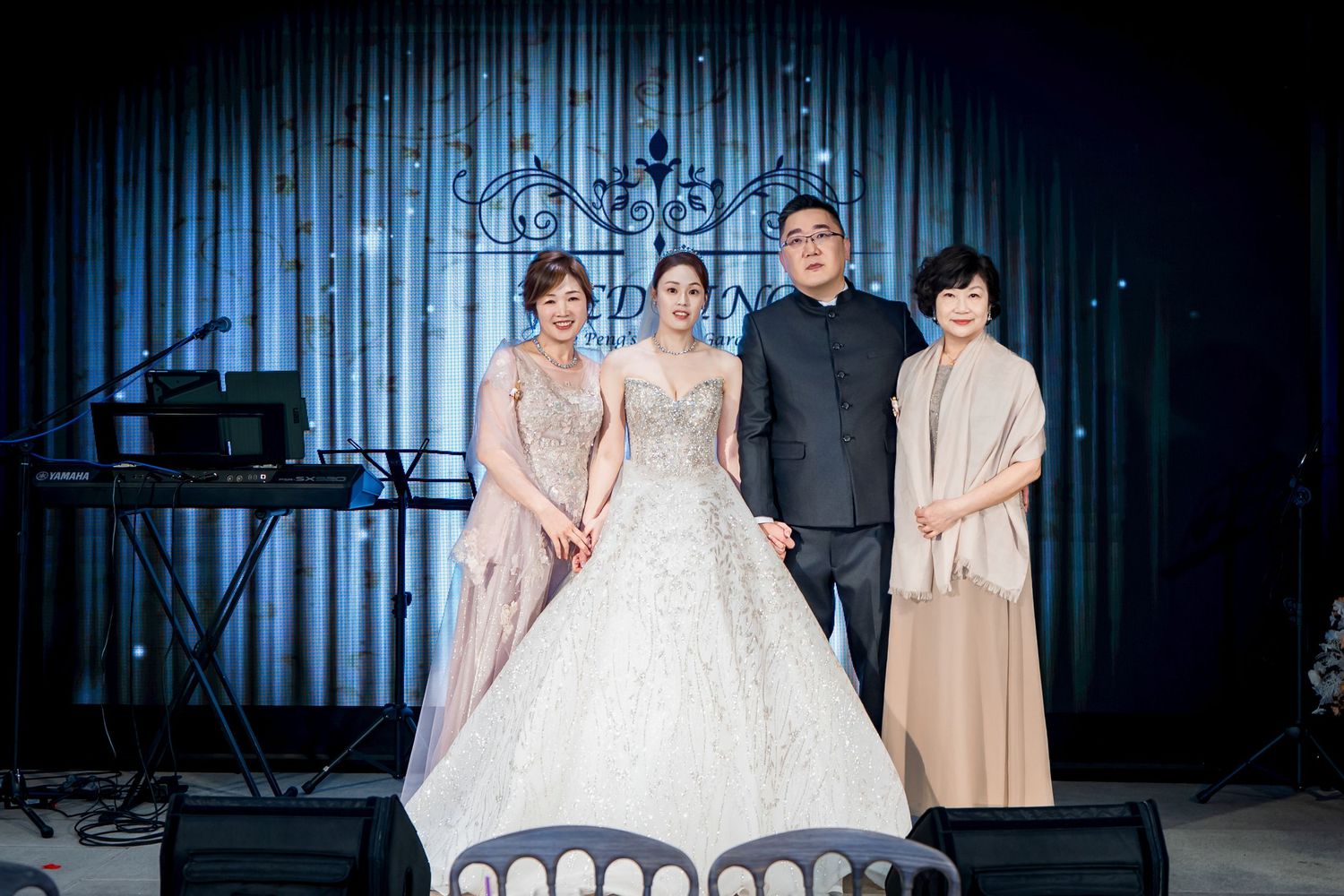 Wedding party poses together in formal attire against a dark blue-lit backdrop at an elegant venue.