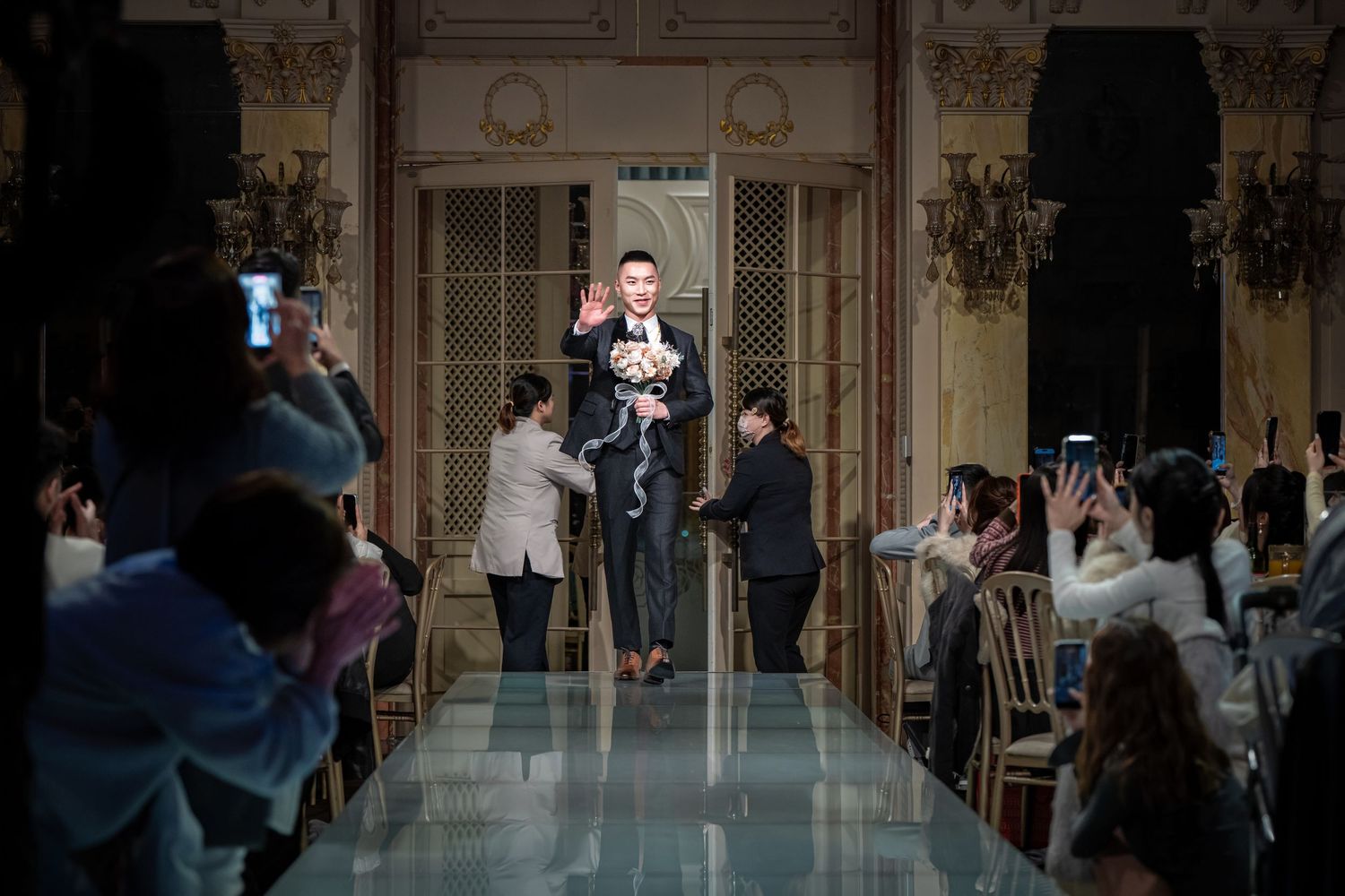 Elegant ballroom scene with couples dancing in formal attire at an upscale venue with ornate chandeliers.