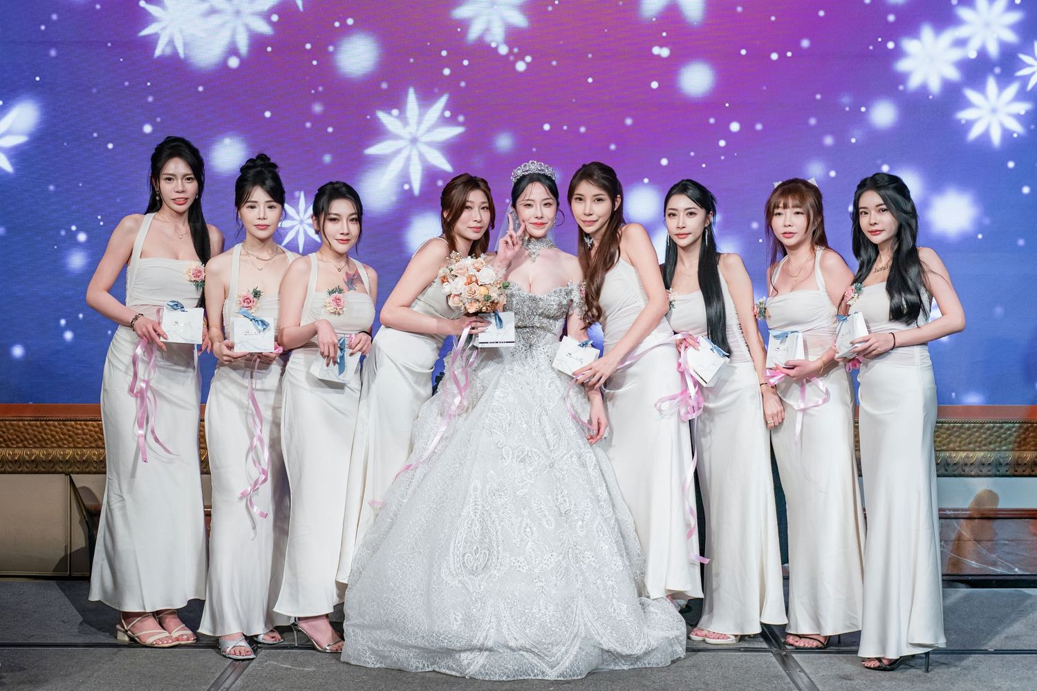 A group of people wearing elegant white dresses pose together for a formal event photograph.
