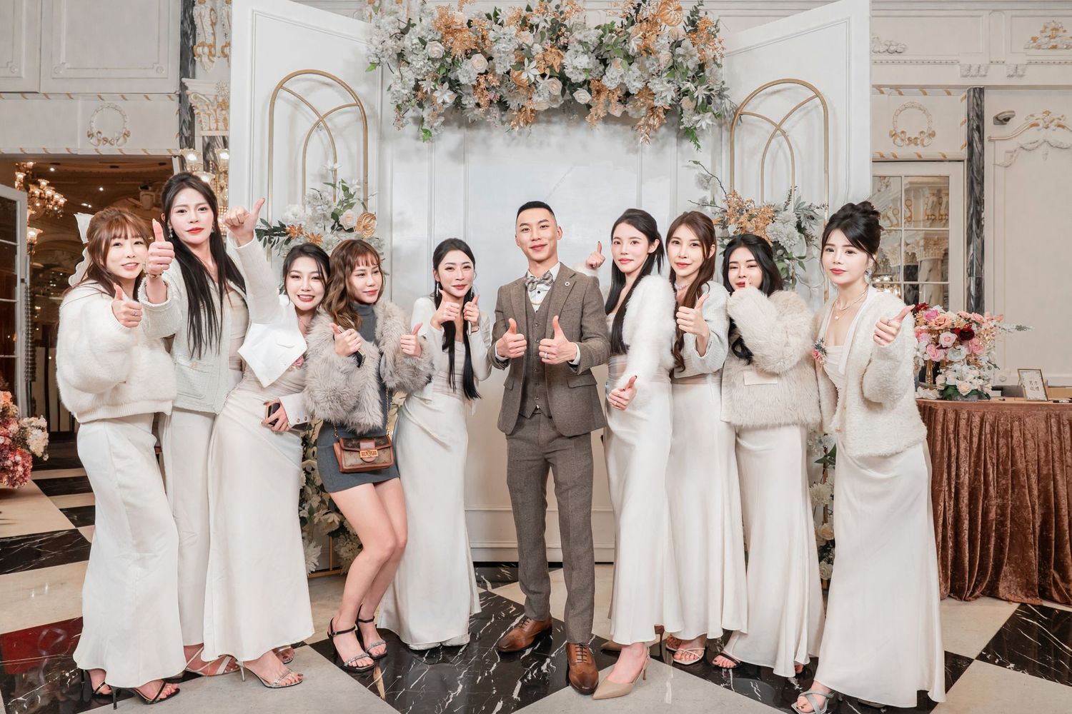Wedding party poses together in an elegant white room decorated with floral arrangements and soft lighting.