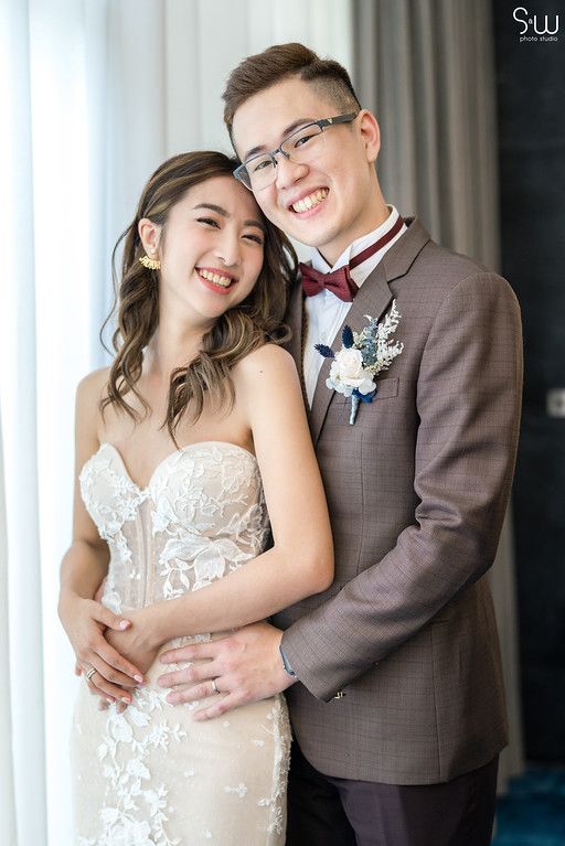 Joyful wedding portrait of couple in formal attire with boutonniere detail.