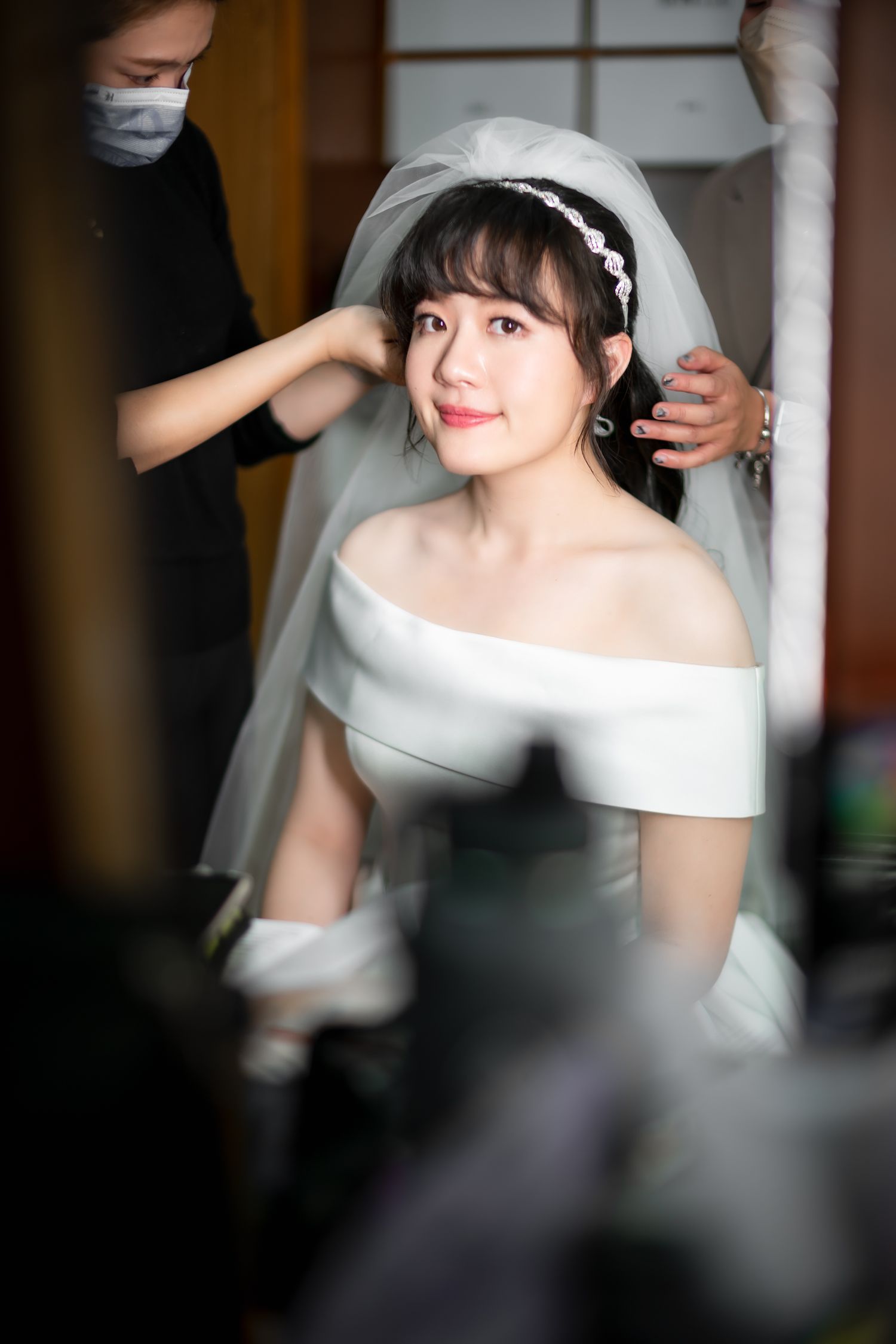 Getting ready shot of a bride in an off-shoulder dress having her veil adjusted.