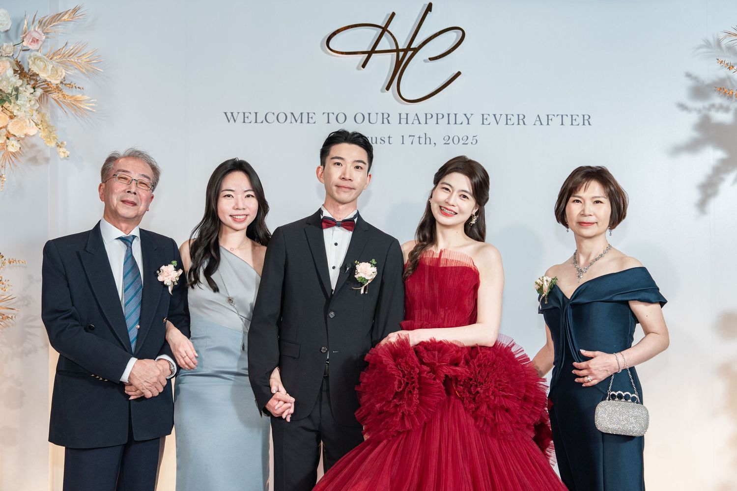 Elegant wedding celebration with formal attire featuring black suits and beautiful red and gray evening gowns.