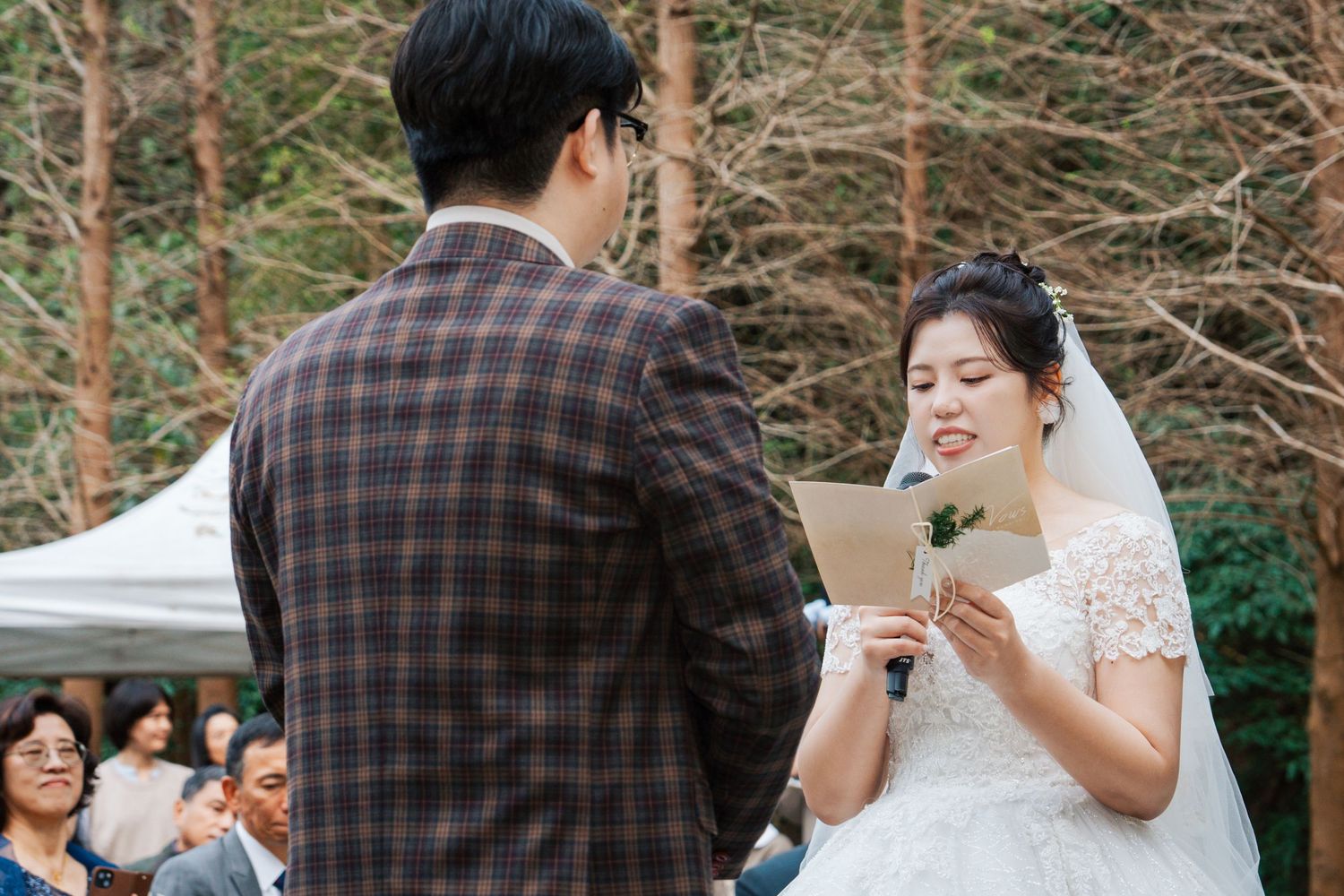 A couple shares an intimate moment during their wedding ceremony in a wooded outdoor setting.