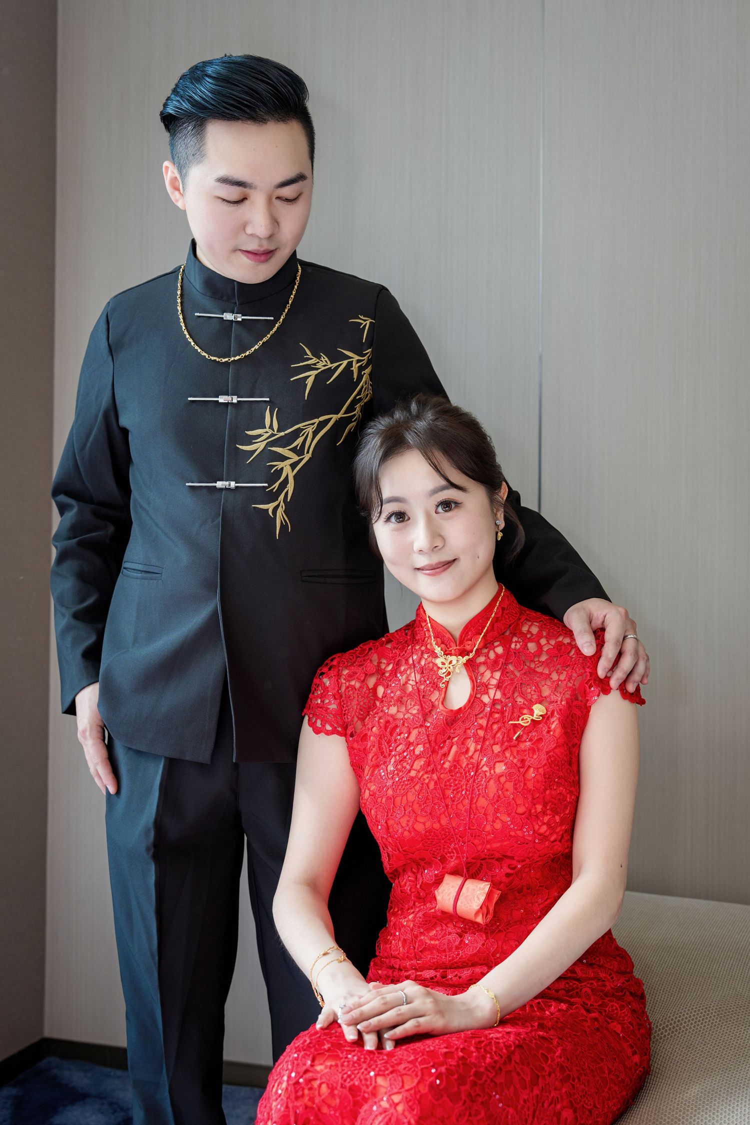 A couple in traditional Chinese formal wear, with the woman in red qipao and man in black suit with gold embroidery.