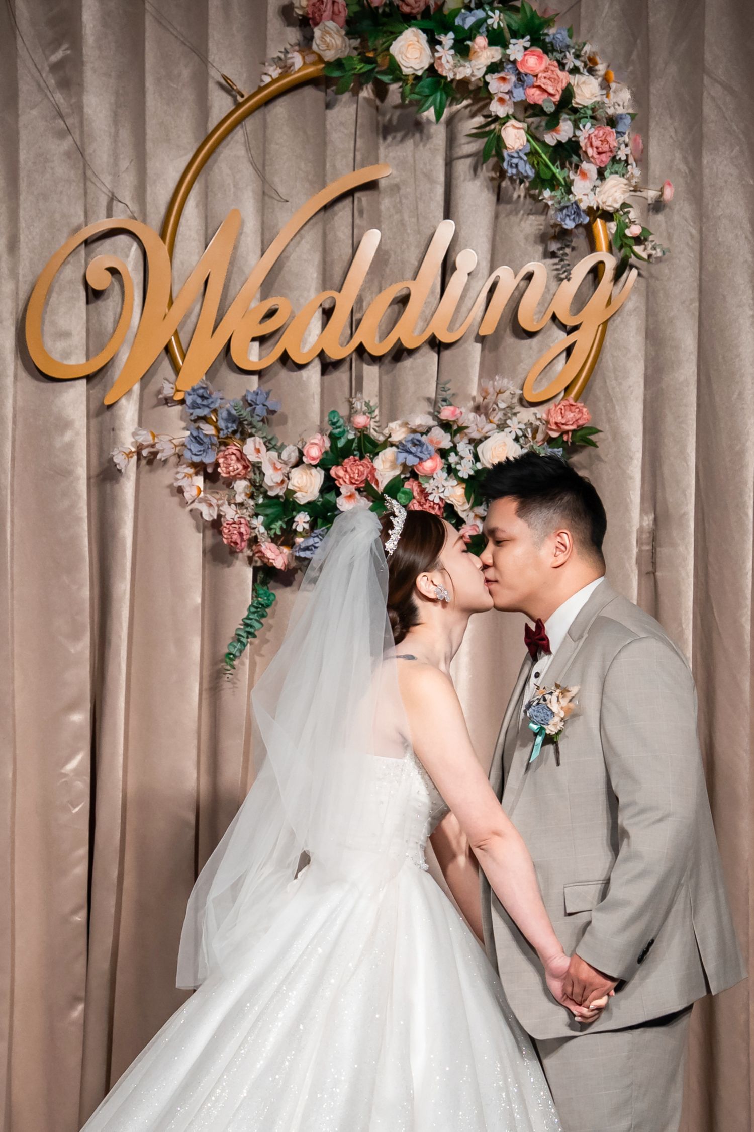 A romantic wedding scene with floral arch decorations and elegant gold lettering against a draped fabric backdrop.