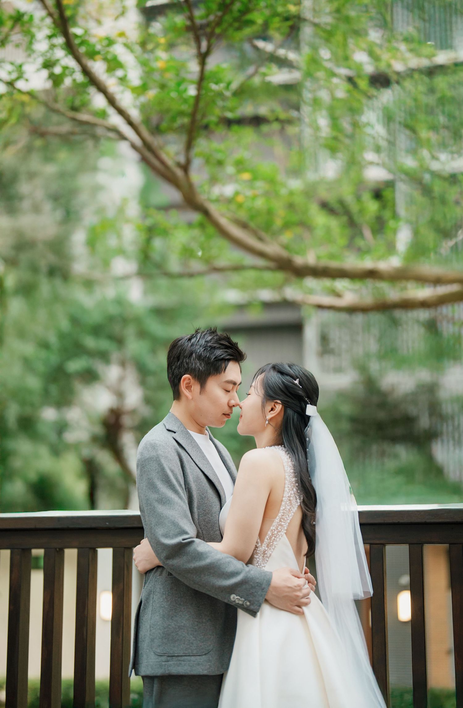 A romantic wedding couple shares intimate moments on a wooden deck surrounded by lush greenery.