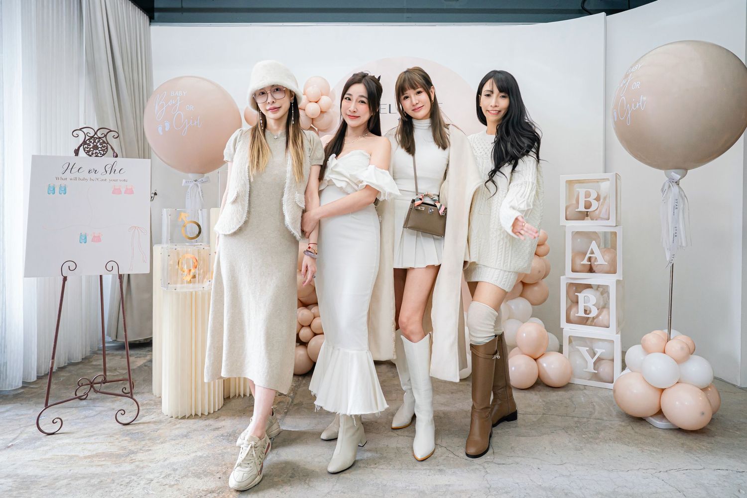 A group in white dresses and outfits poses together in a bright studio space with neutral balloon decorations.