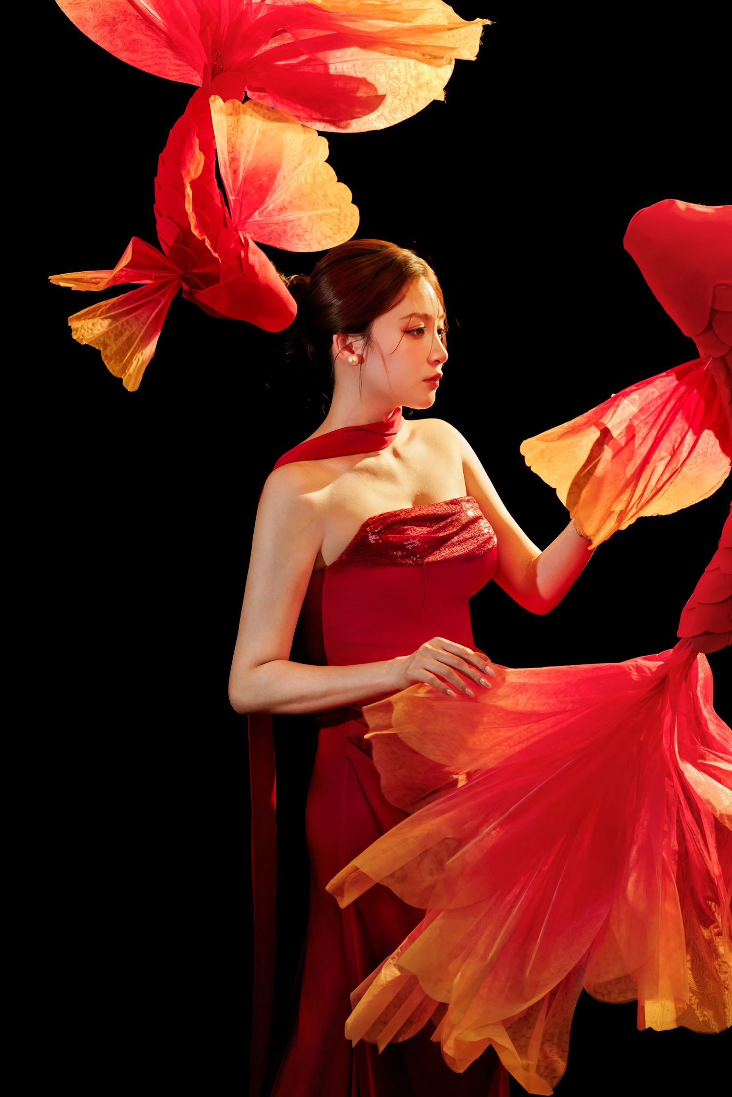 Woman in red gown surrounded by large red and yellow flower petals on black background.