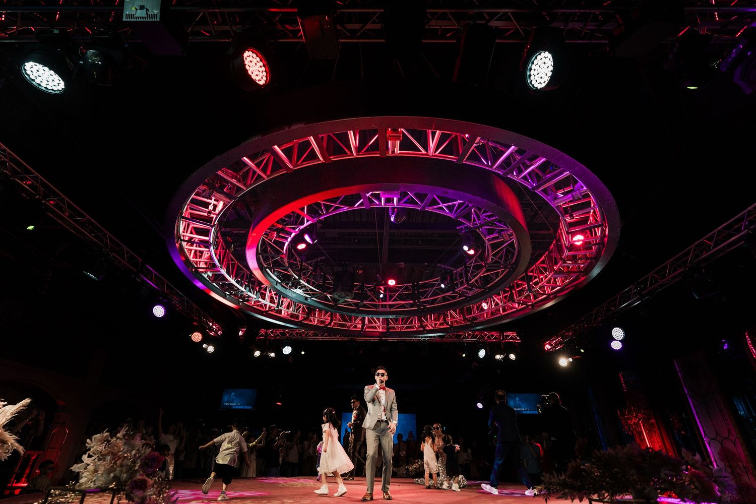 Performers on a circular stage beneath a large illuminated red ring during a theatrical show.