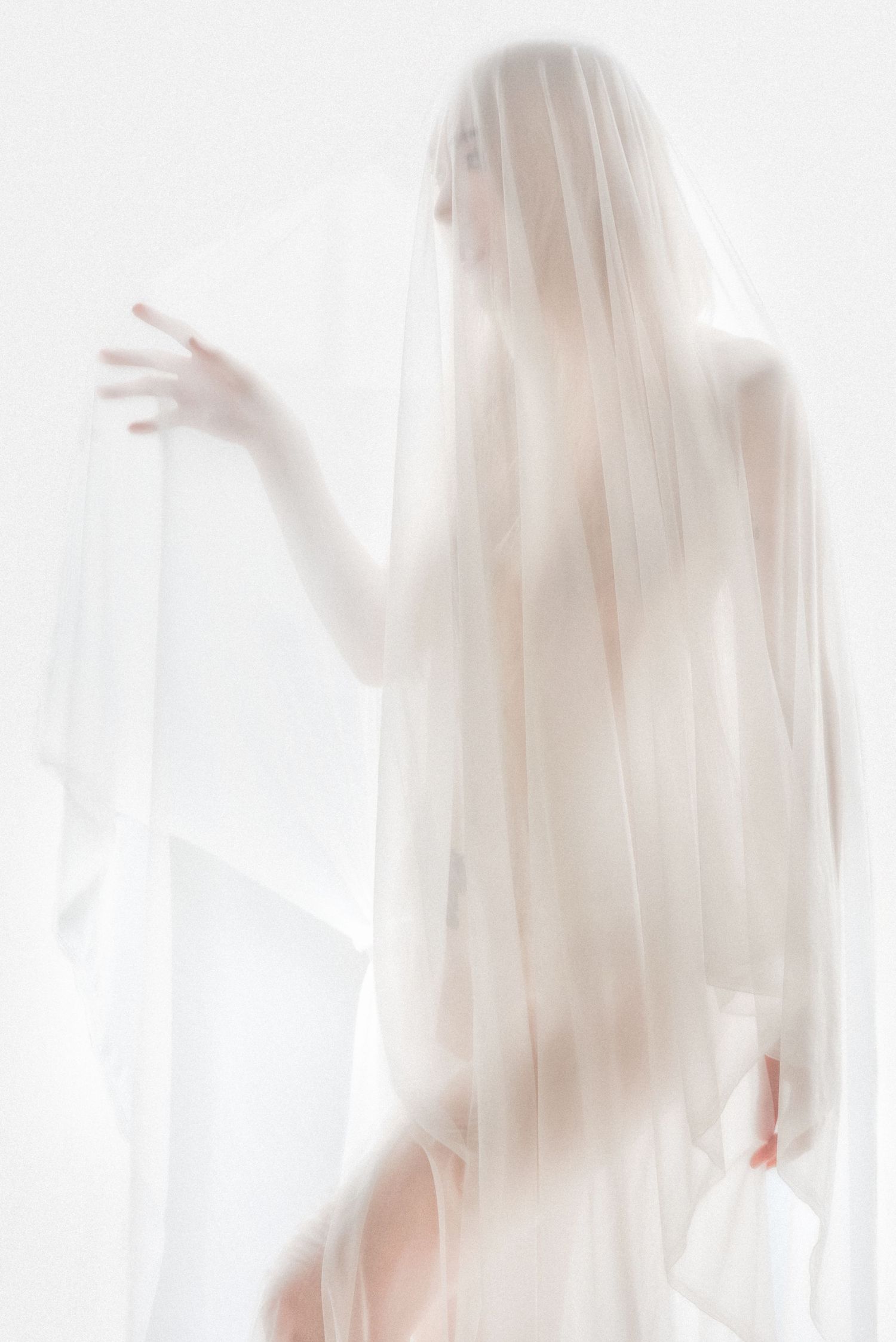 Ethereal silhouette figure draped in sheer white fabric poses gracefully against bright background.