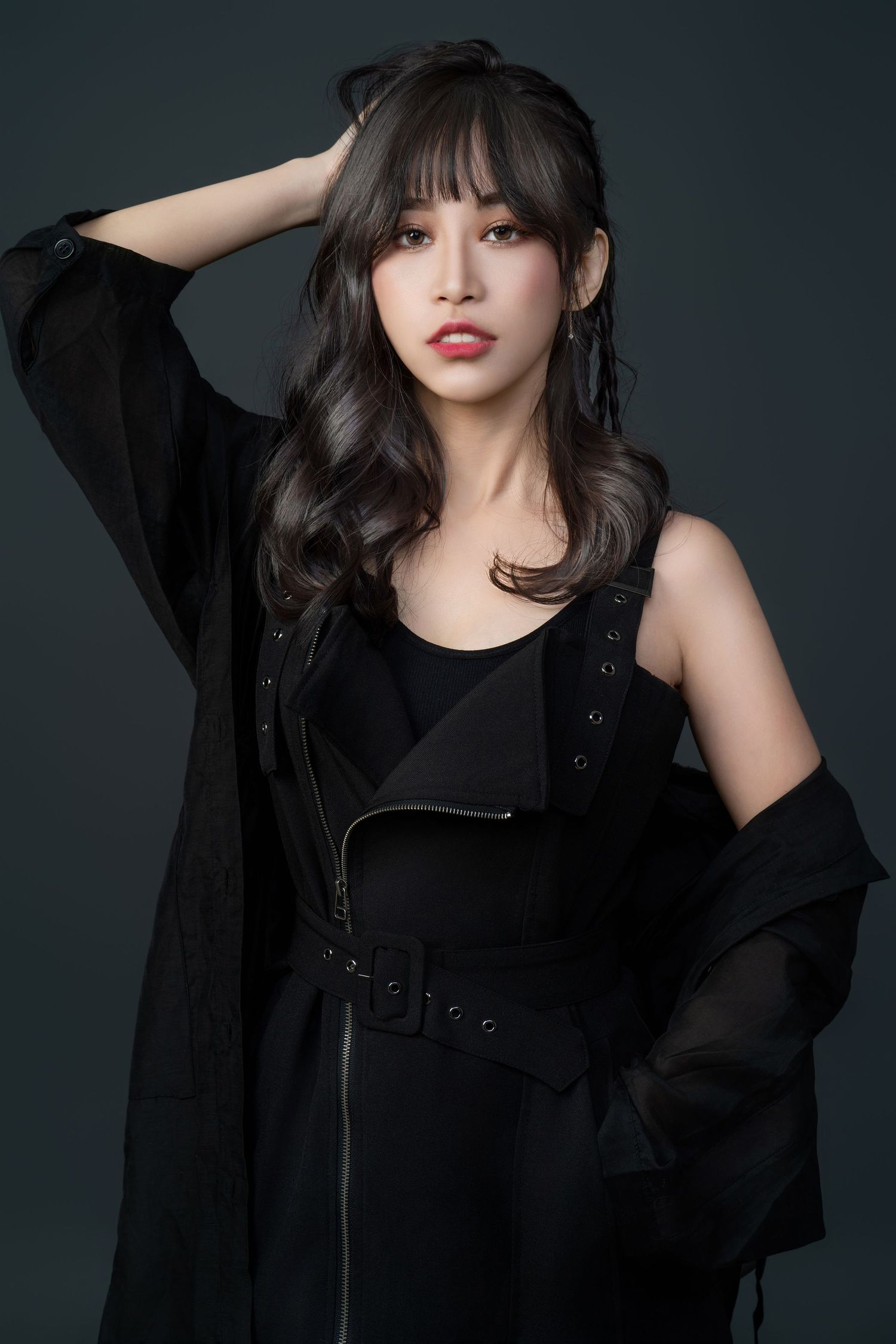 Studio portrait with dark background featuring elegant all-black outfit with sheer jacket and red lips against gray backdrop.