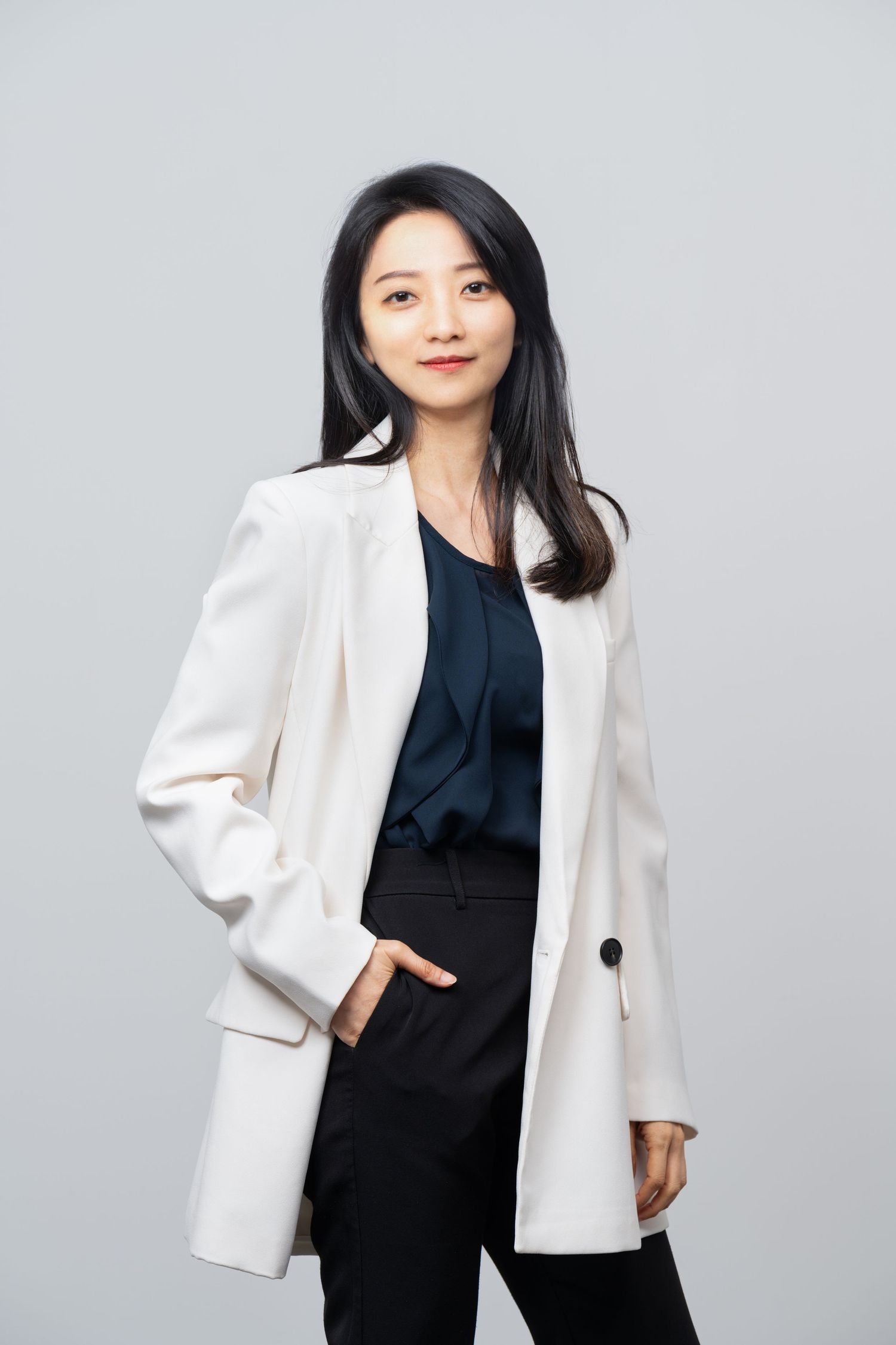 Professional business attire featuring a white blazer, dark top and trousers against a light gray studio background.
