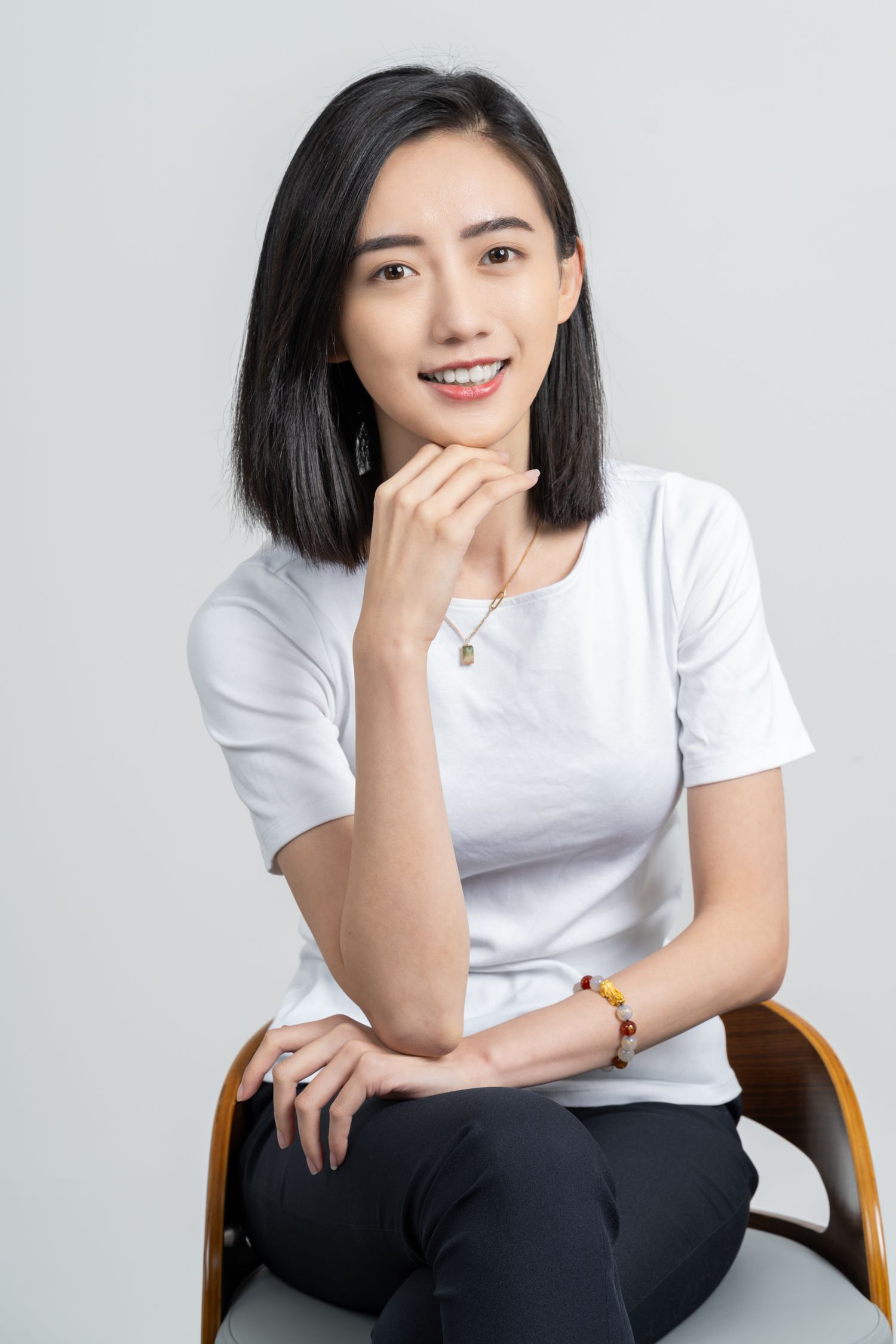A portrait of someone wearing a white t-shirt sitting casually in a chair against a gray background.