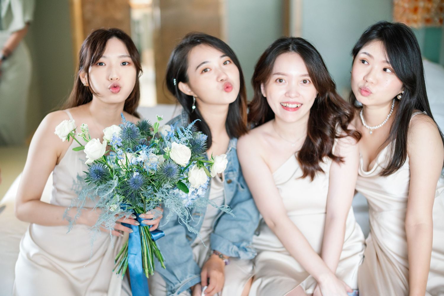 Four bridesmaids in flowing pastel dresses pose together at a wedding with one holding a blue and white bouquet.