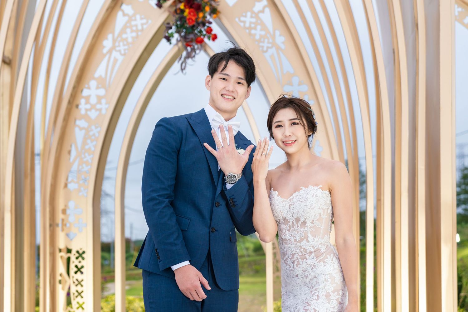 A couple poses under an elegant arched chapel doorway decorated with flowers on their wedding day.