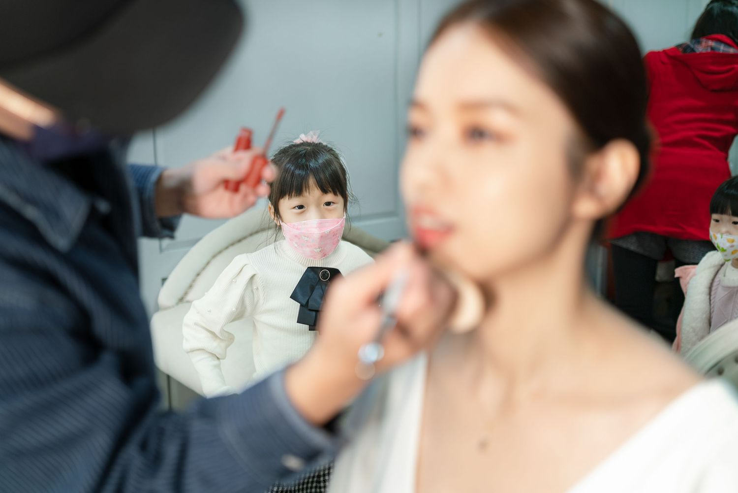 Behind the scenes view of makeup artists working on models in a preparation area before a show or photoshoot.