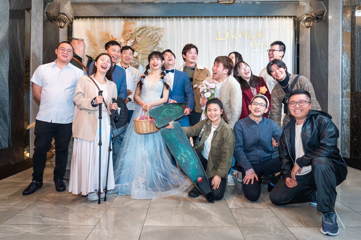 A wedding celebration group photo showing people in formal attire with the couple in elegant blue and white gowns.