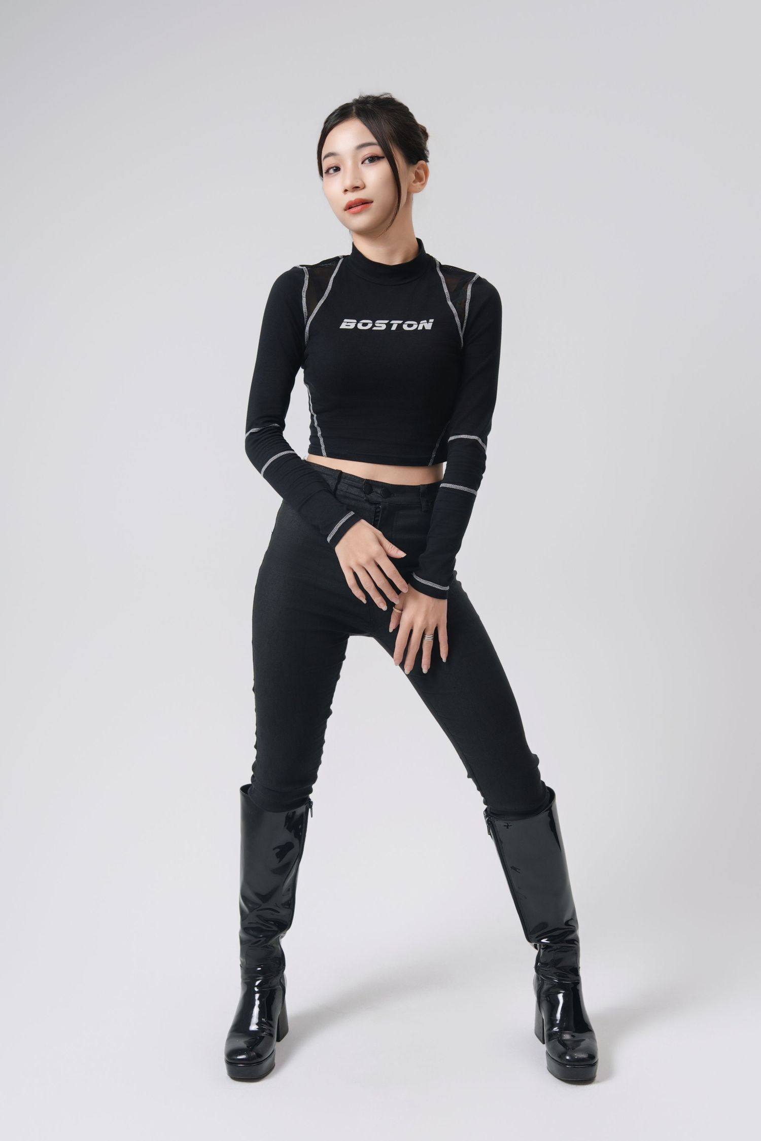 Athletic figure in black activewear and boots poses dynamically against white background in fashion photoshoot series.
