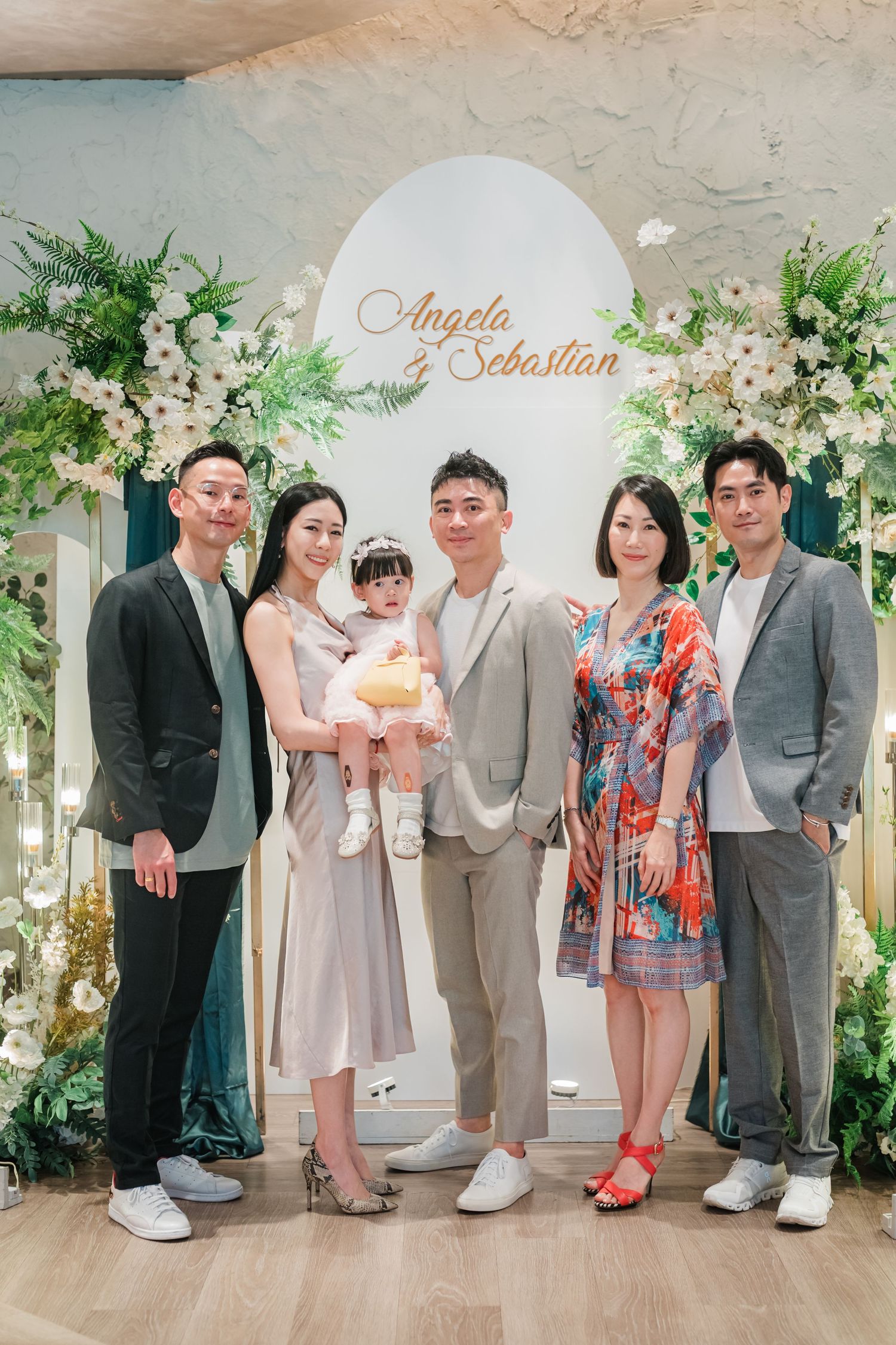 A series of family portraits with multiple generations gathered in front of a white floral backdrop at a formal event.