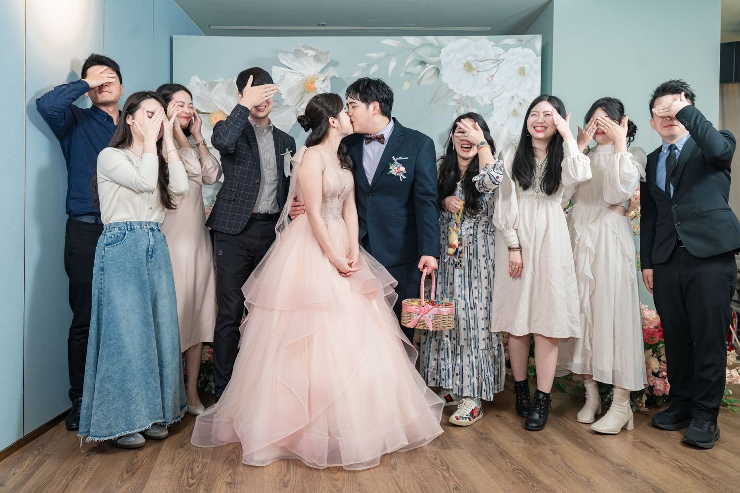 Wedding guests gather for formal photos in a blue-walled room with floral decorations.