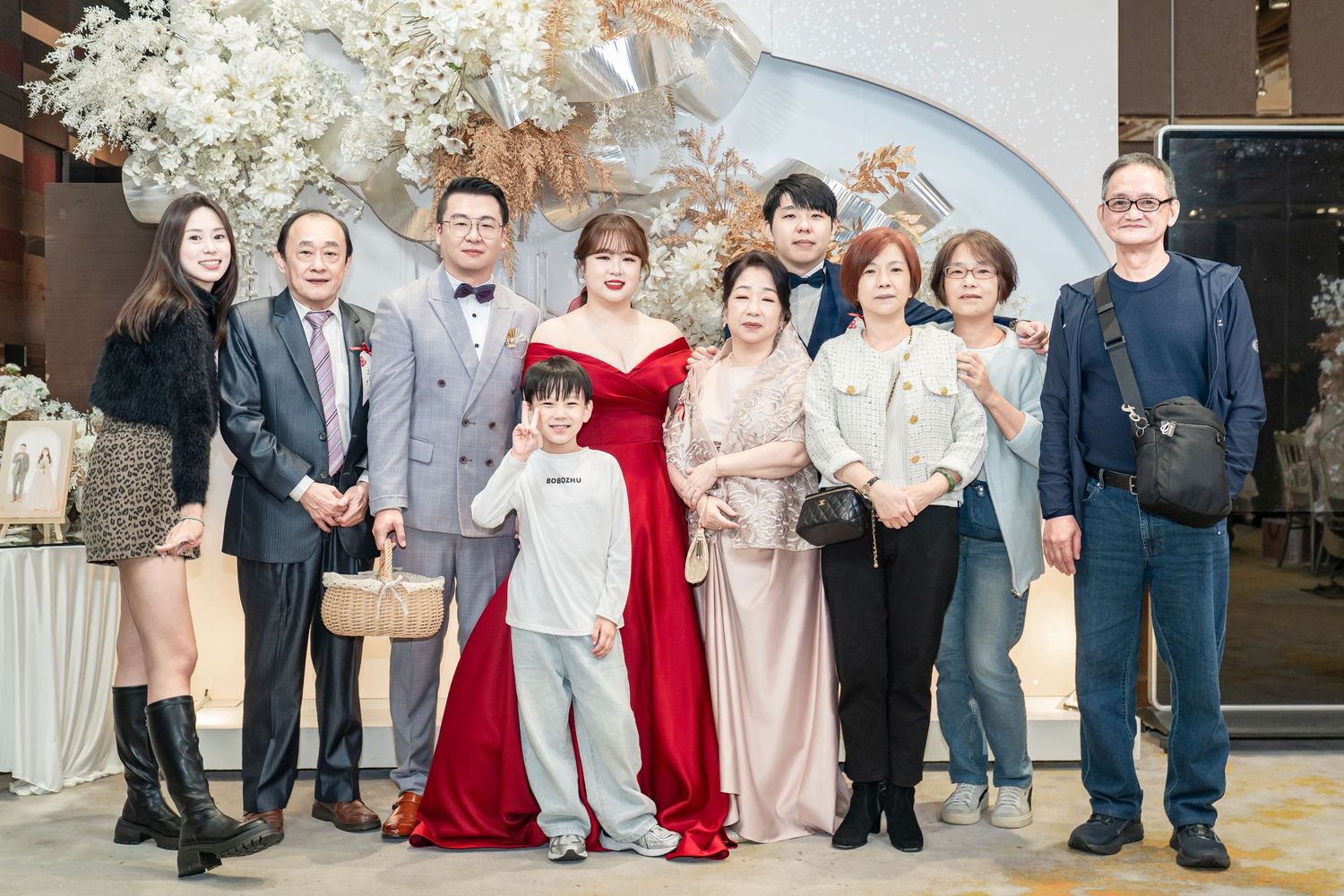 Wedding guests pose together in formal attire at an elegant reception venue with white floral decorations.