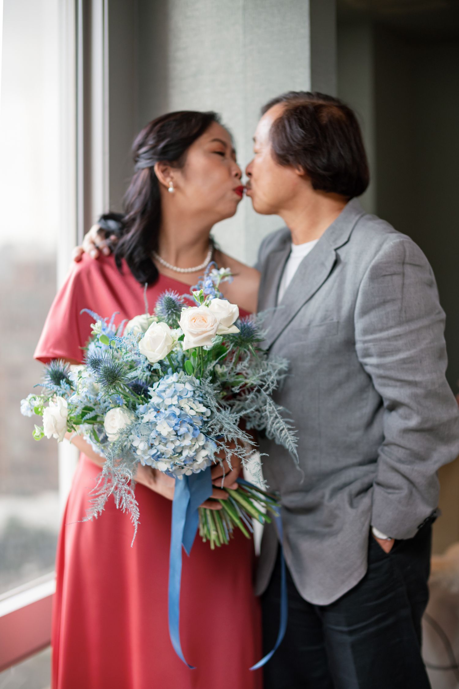 A romantic couple shares a kiss while holding a beautiful bouquet of white roses and blue hydrangeas with a blue ribbon.