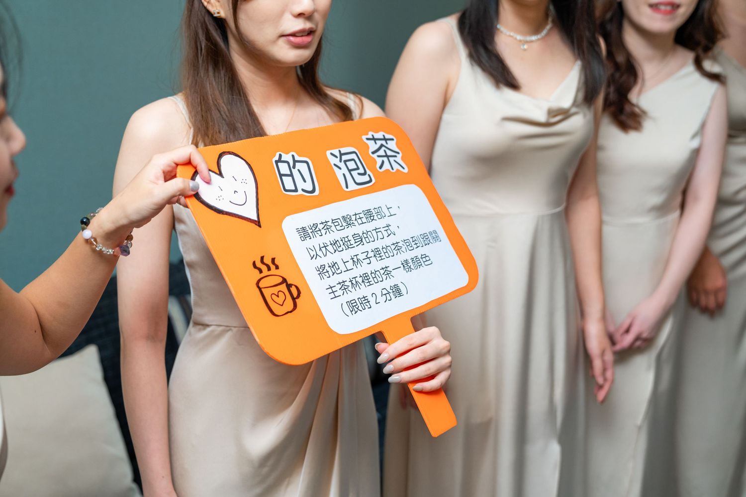 Wedding party members in beige dresses hold up an orange sign with Chinese text and cartoon heart illustrations.