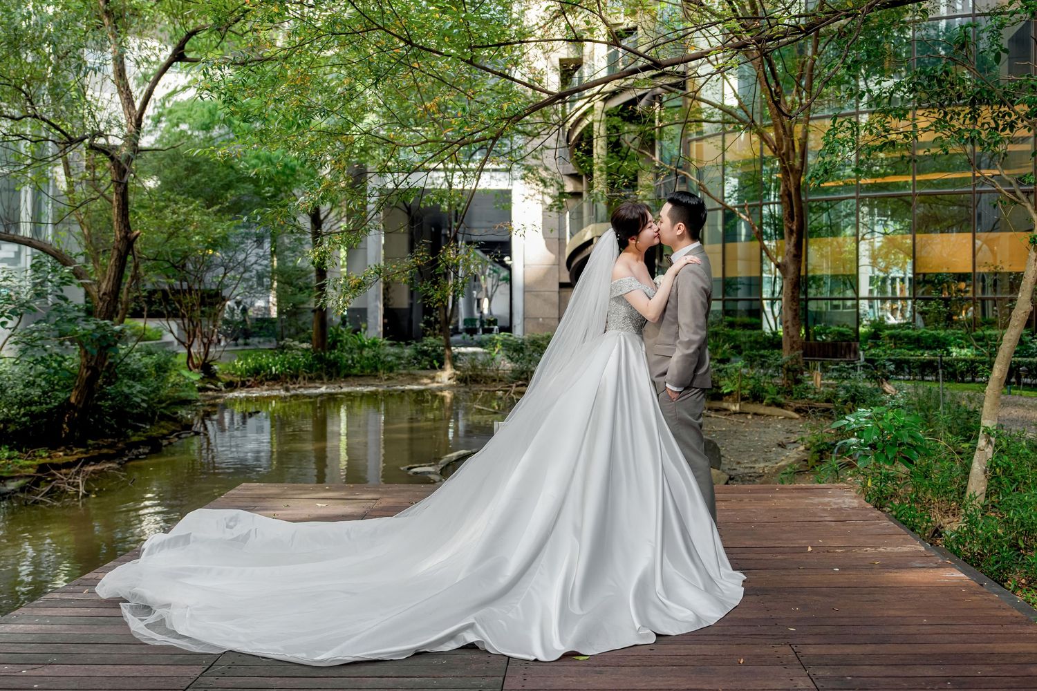 A couple shares a romantic moment in a lush garden setting with a flowing white wedding dress trailing behind them.