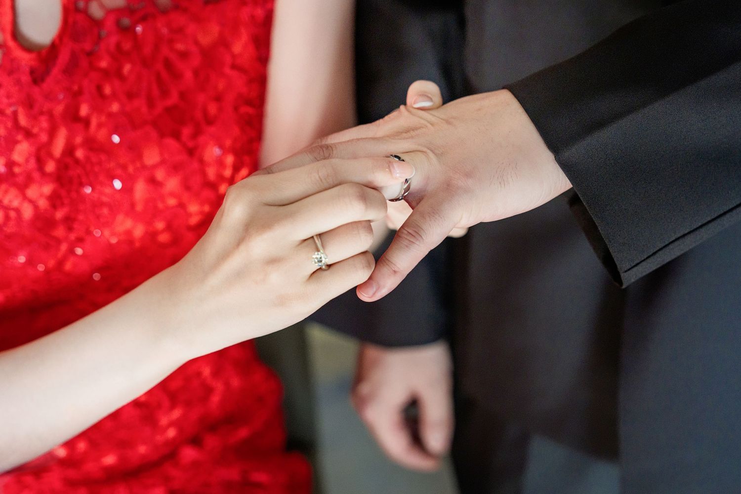 A sequence of hands exchanging rings during a wedding ceremony against a red and black background.