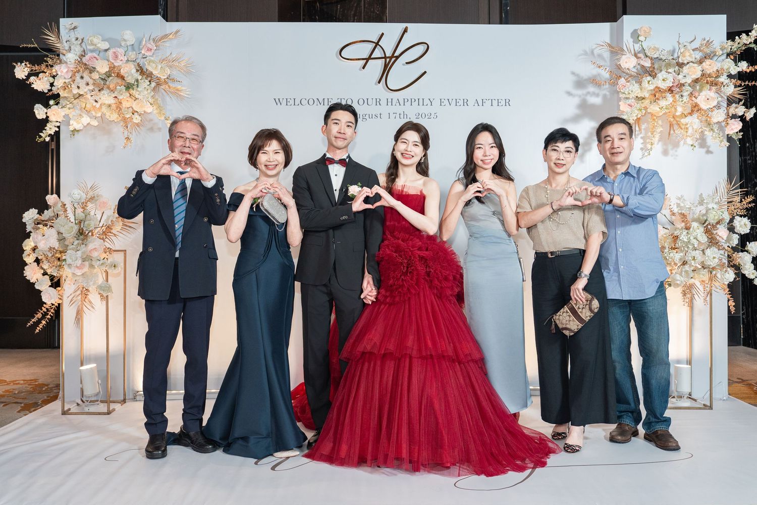 Elegant wedding party poses in front of a floral arch backdrop with gold decor and monogram signage.