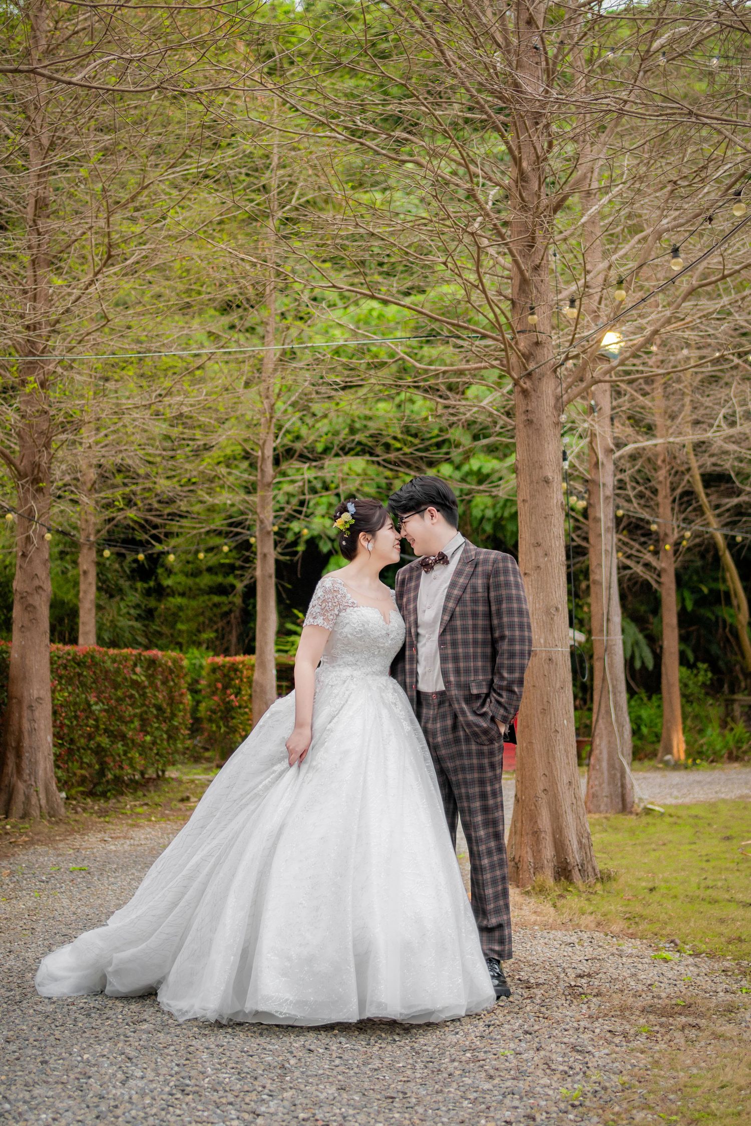 A romantic couple in wedding attire shares intimate moments among tall trees in a wooded outdoor setting.