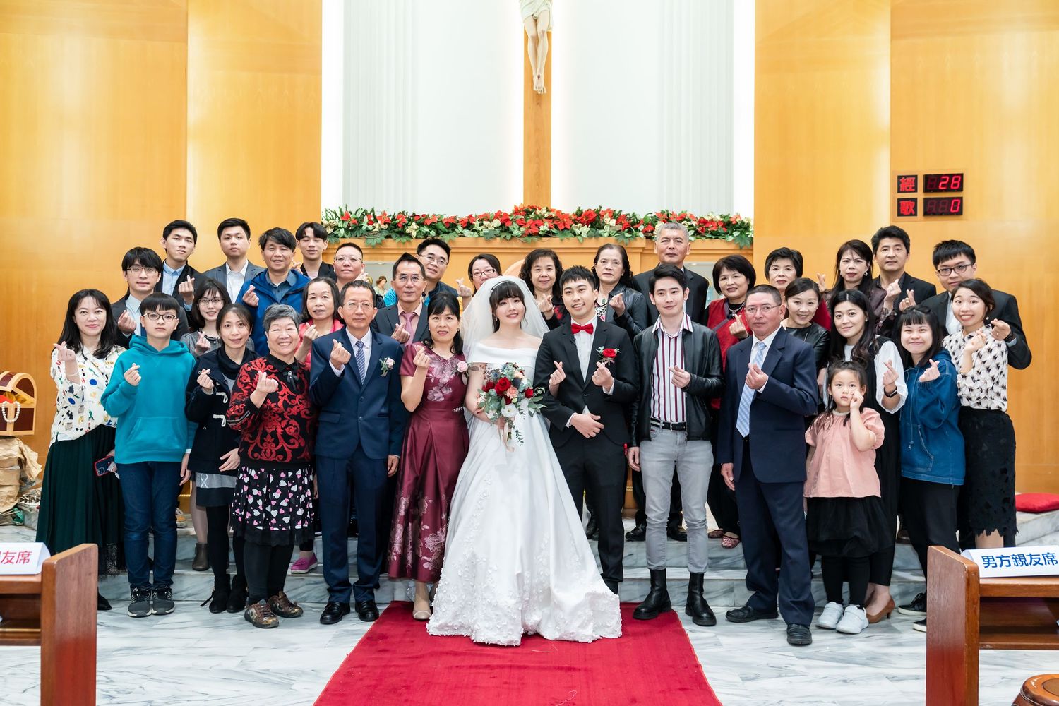 Large wedding group photo in church with golden walls and red carpet.