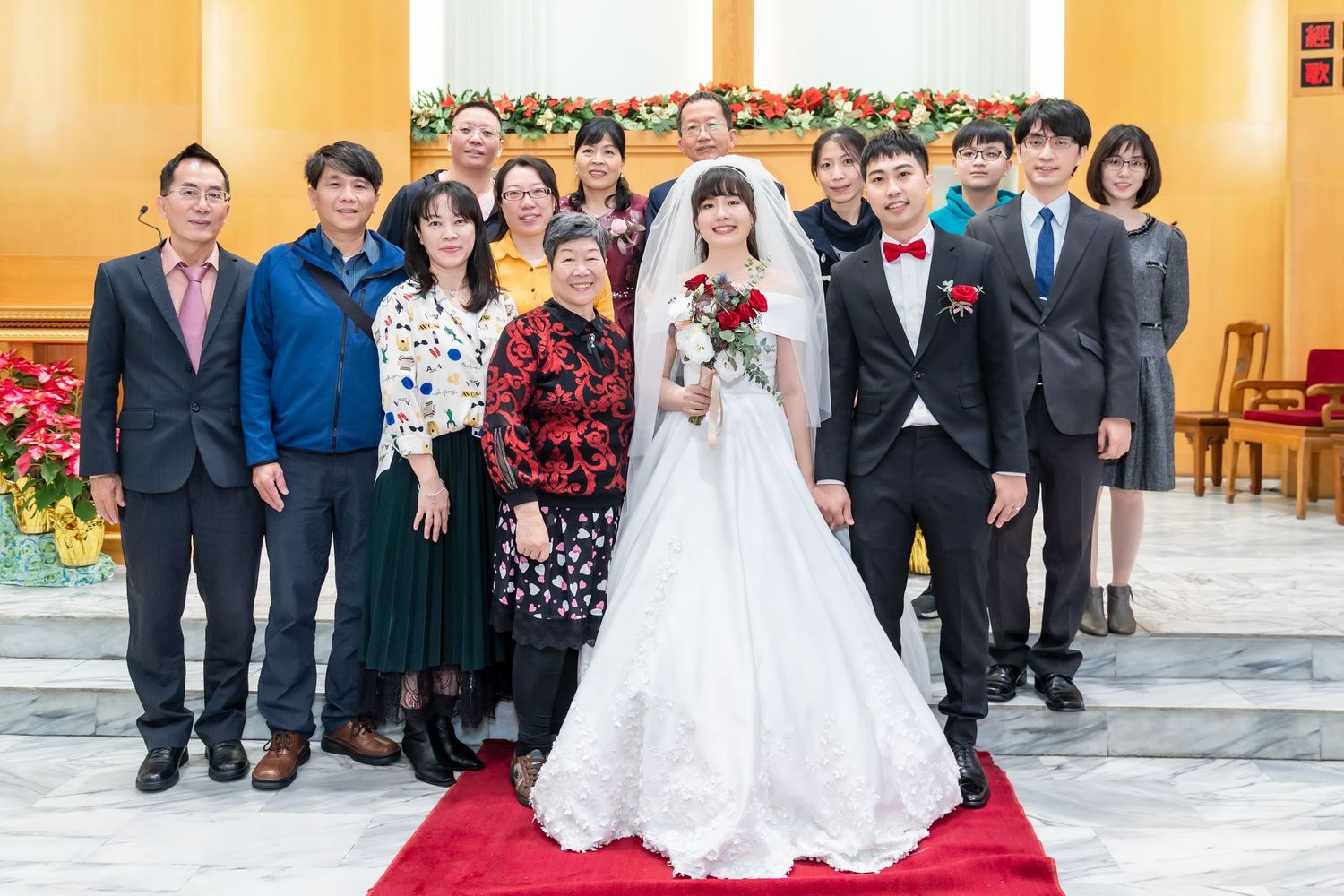 Wedding party and family members gather for formal photo on red carpet.