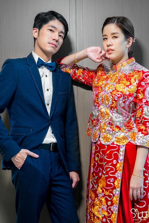 Stylish couple in navy tuxedo and red Chinese traditional wedding dress posing for portrait.