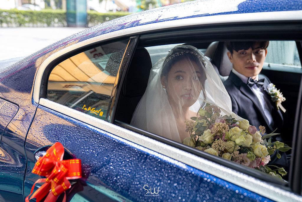 A wedding couple inside a decorated car with a red bow during their special day.