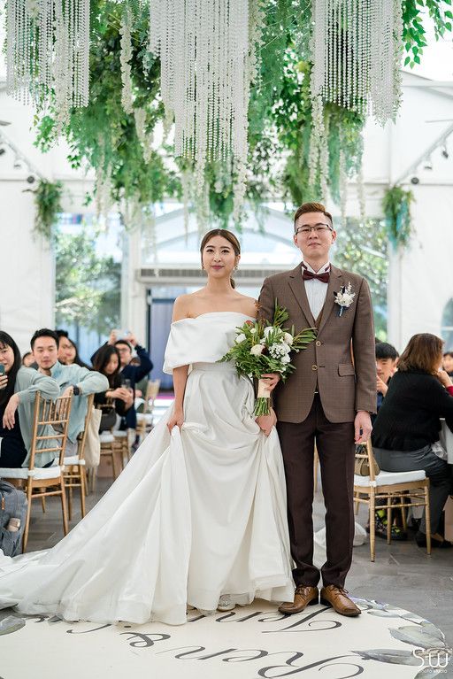 Elegant wedding ceremony in a greenhouse-style venue with hanging greenery and crystal decorations.