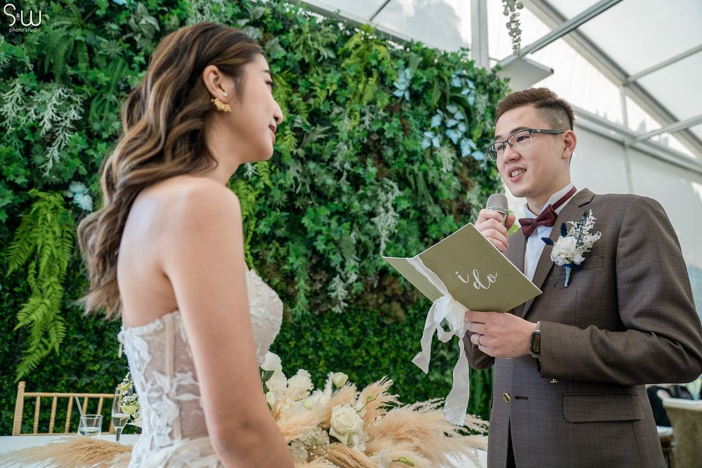 Wedding couple exchanges vows against a backdrop of cascading greenery and white flowers.