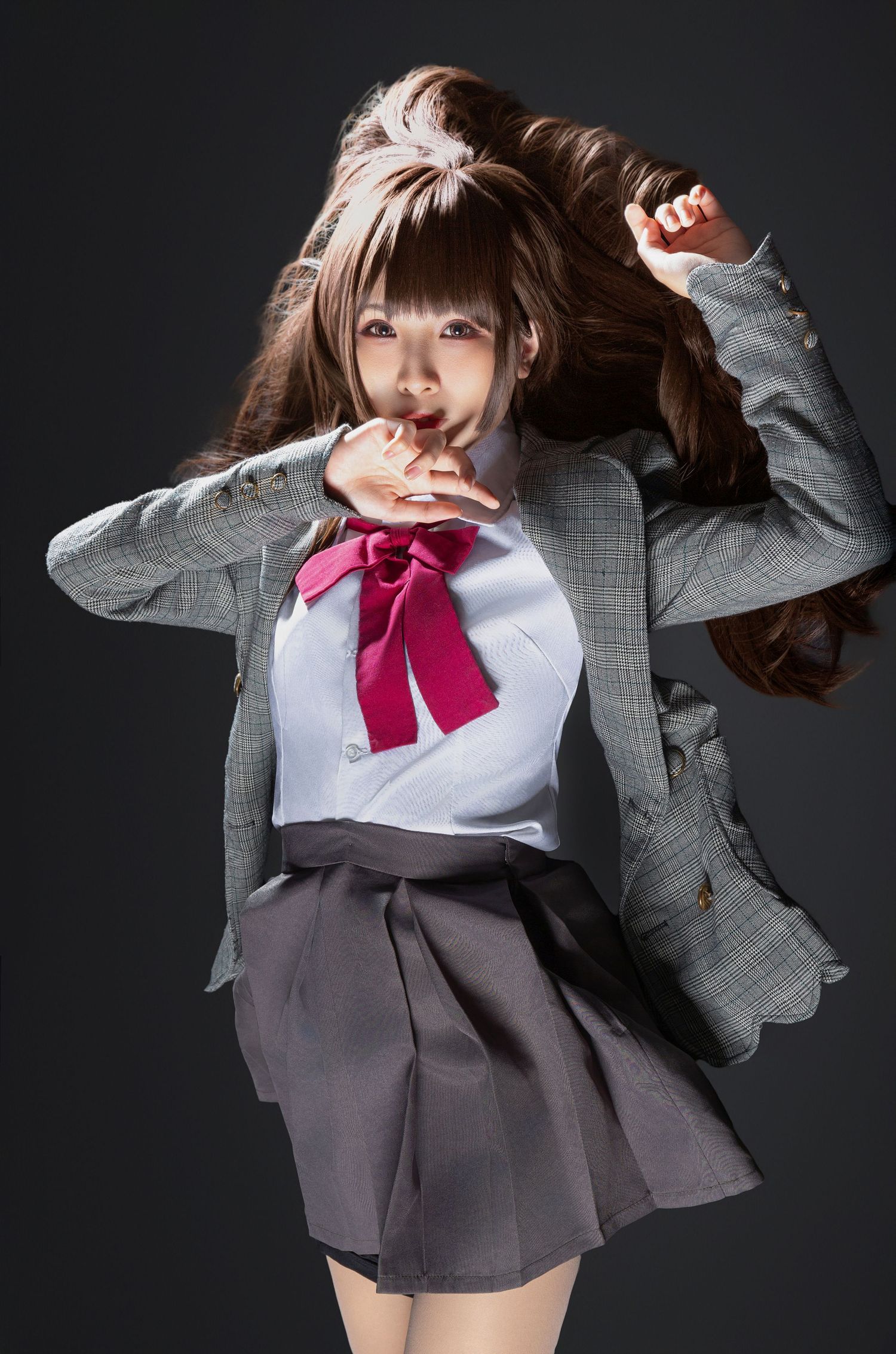 Dramatic studio shot showing a person in school uniform with gray blazer and pink bow leaping with flowing hair against dark background.