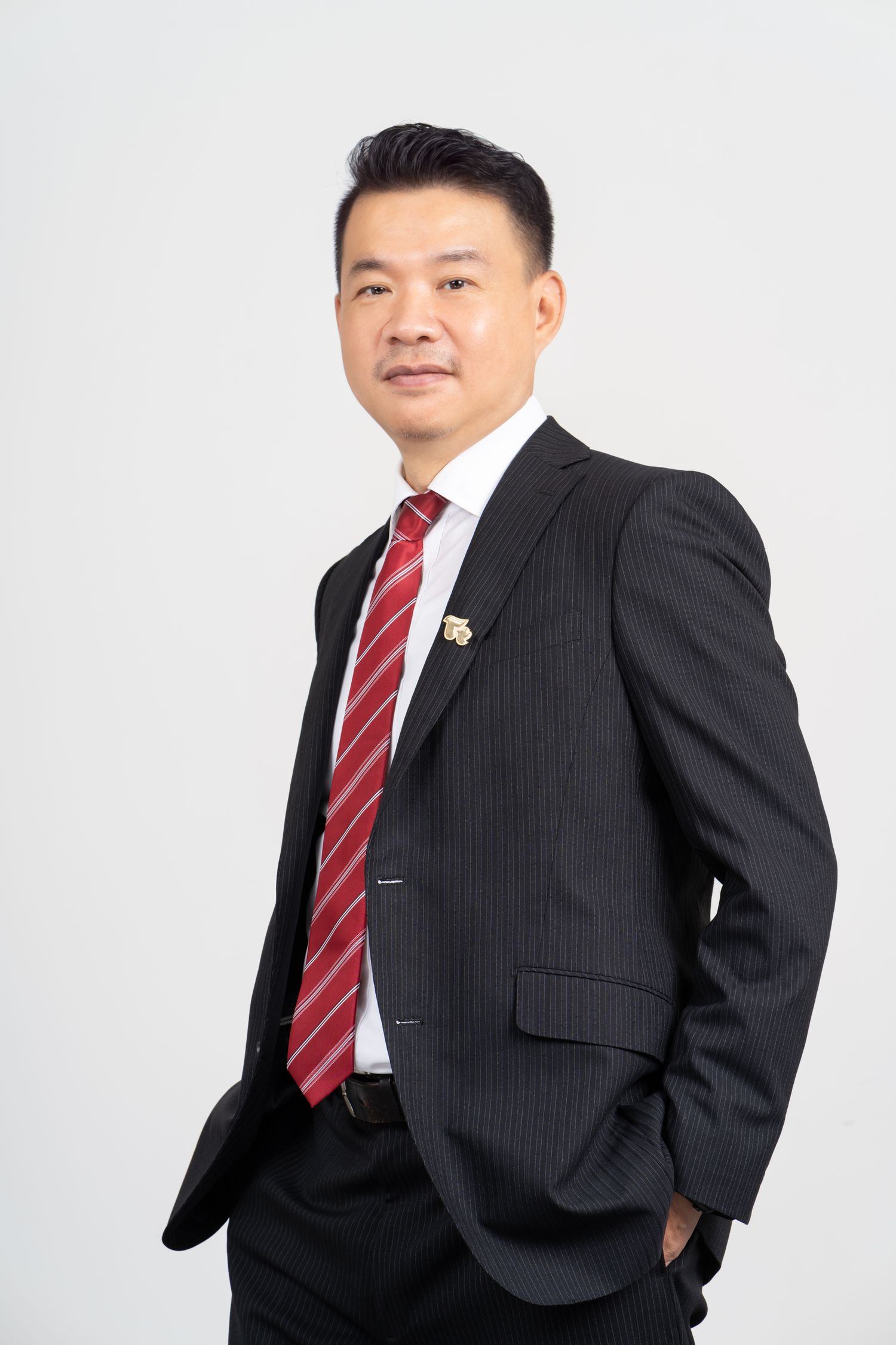 Professional business portrait of an Asian man in a black pinstripe suit with red striped tie on light gray background.