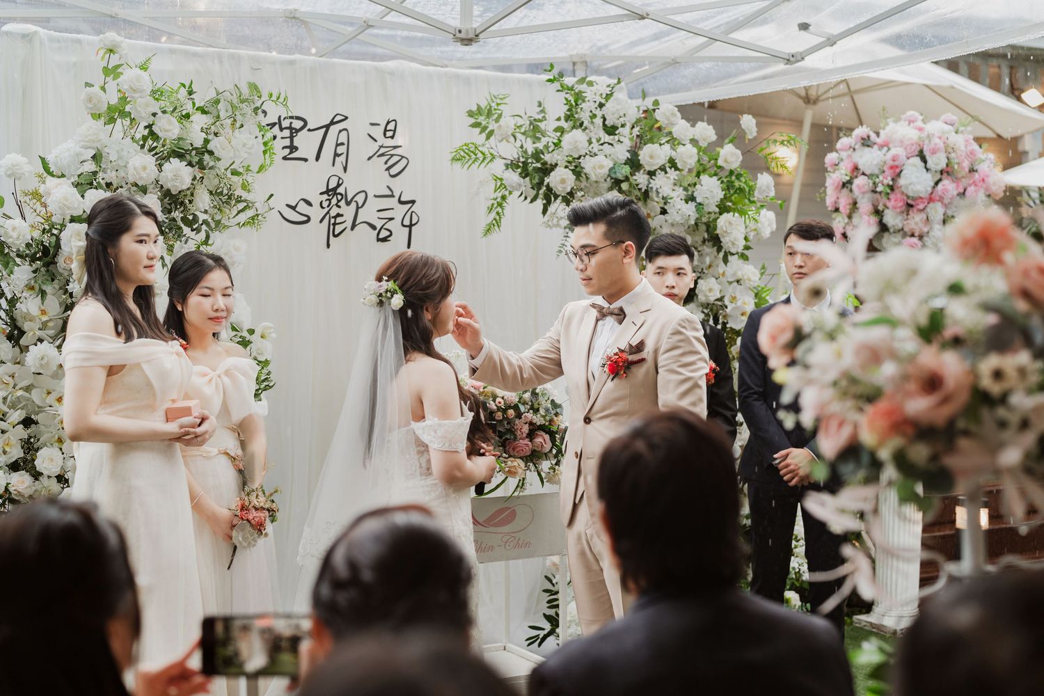 An elegant outdoor wedding ceremony setup with floral decorations and a white canopy tent on a sunny day.