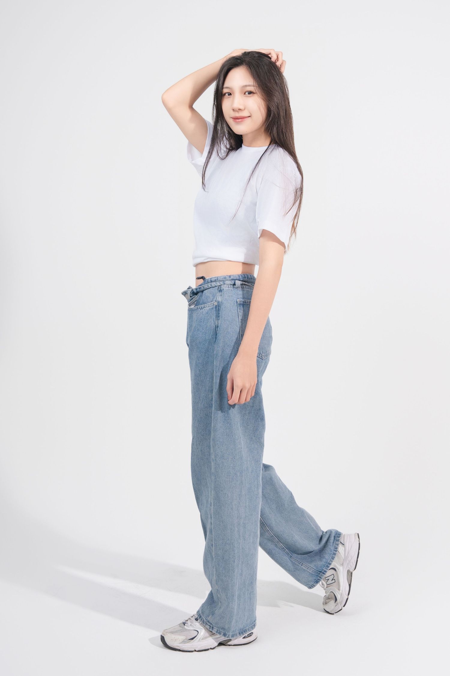 A person wearing a white crop top and baggy light blue jeans poses in different angles against a white background.