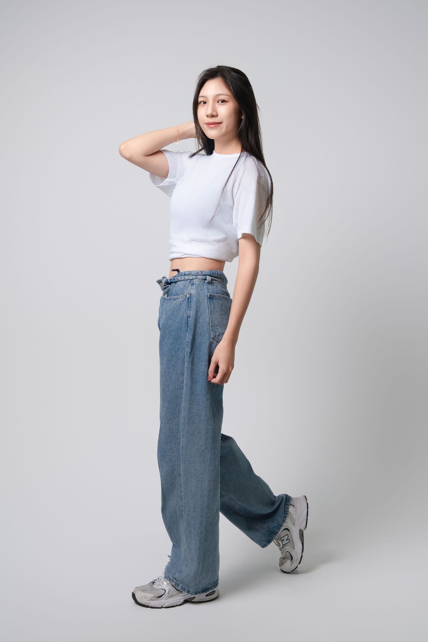 Model in white crop top and baggy jeans poses against gray background showing different angles of the outfit.